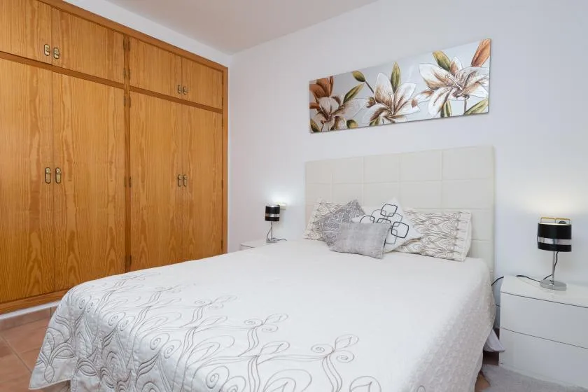 A bedroom with a bed, wooden wardrobes, and floral artwork above the headboard.
