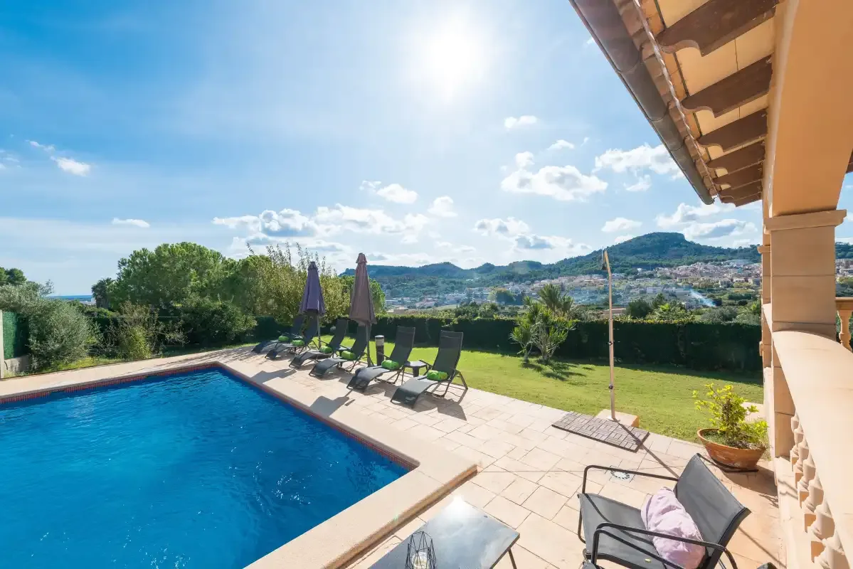 An outdoor pool beside a sunlit patio with loungers and a hillside view.