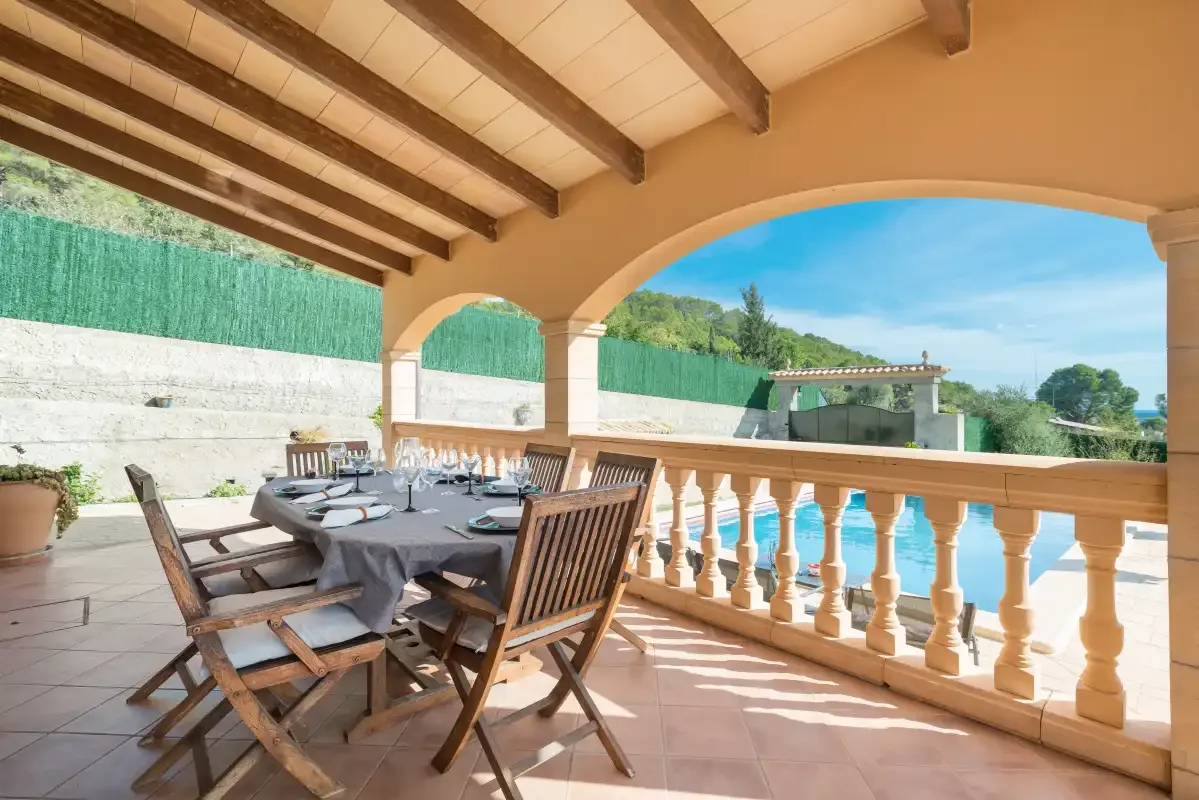 A covered outdoor dining terrace with a long table and wooden seating.