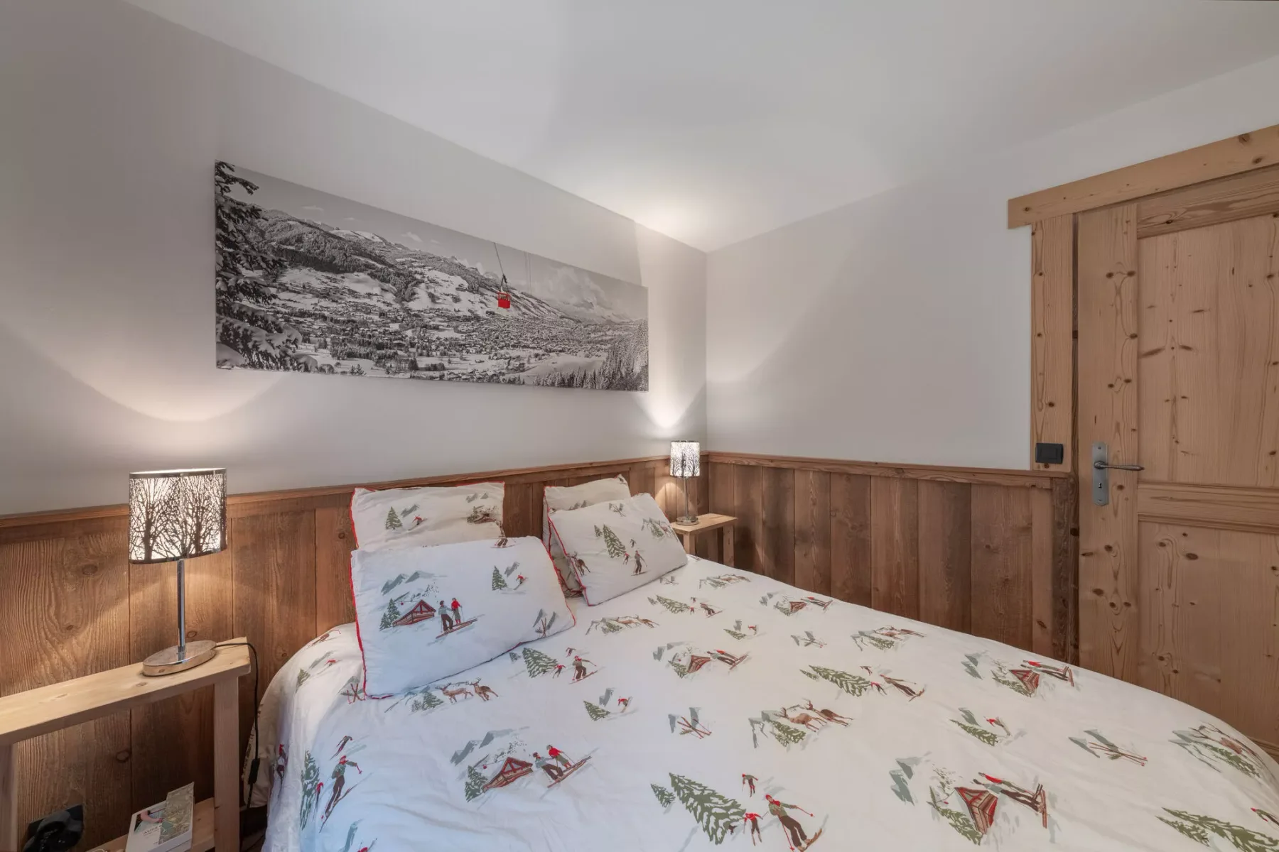A bedroom with a bed dressed in patterned bedding and wood-paneled walls.