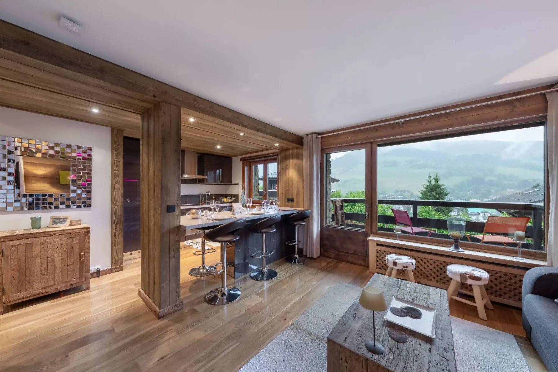 Una sala de estar diáfana con isla de cocina y grandes ventanales hacia un balcón.