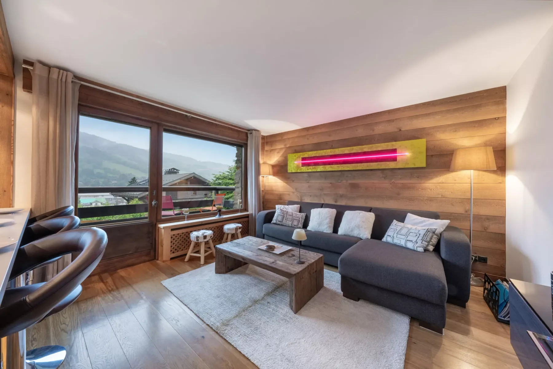 Una sala de estar con sofá seccional, mesa de centro y grandes ventanas.