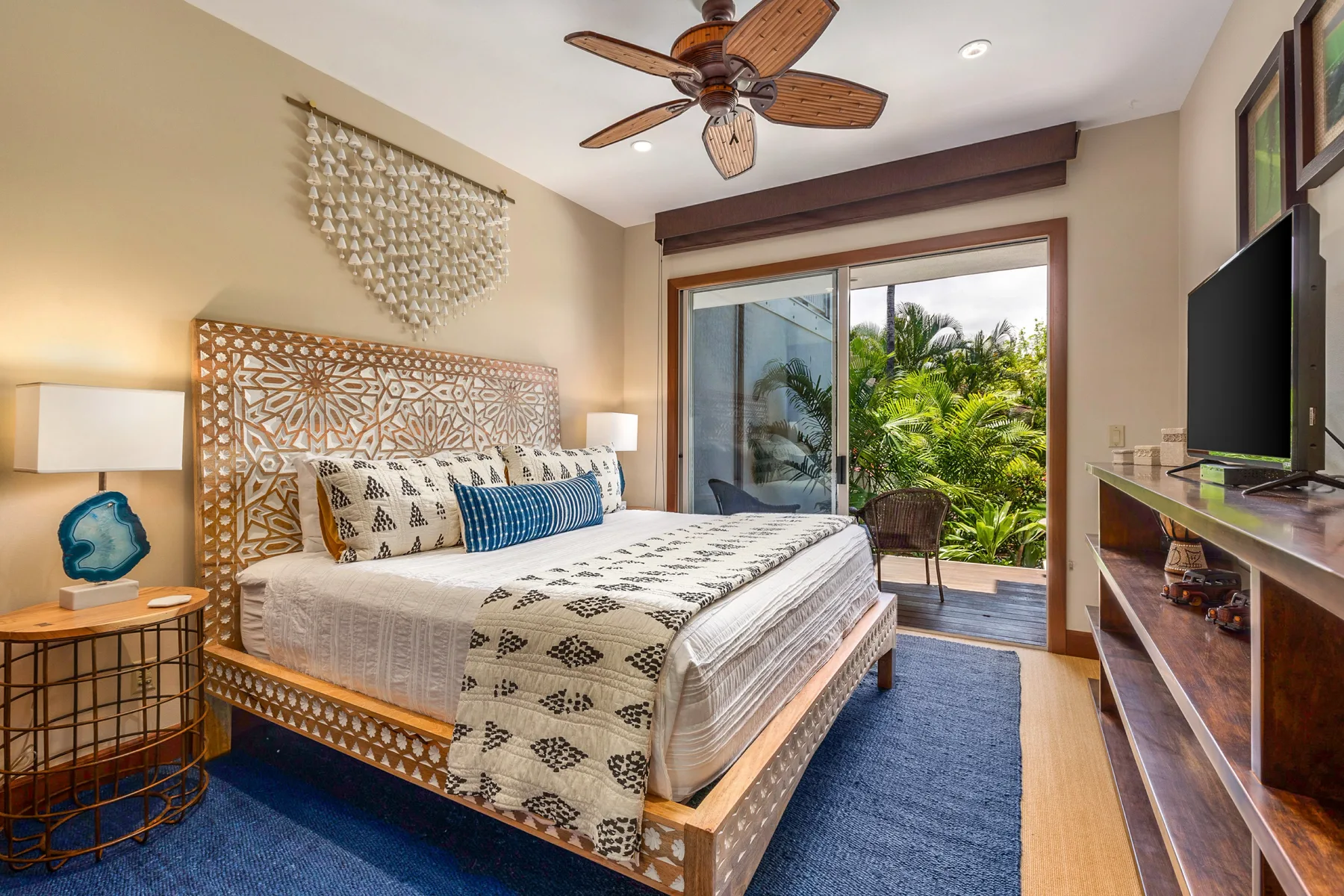 A bedroom with a patterned bed and sliding glass doors opening onto greenery.