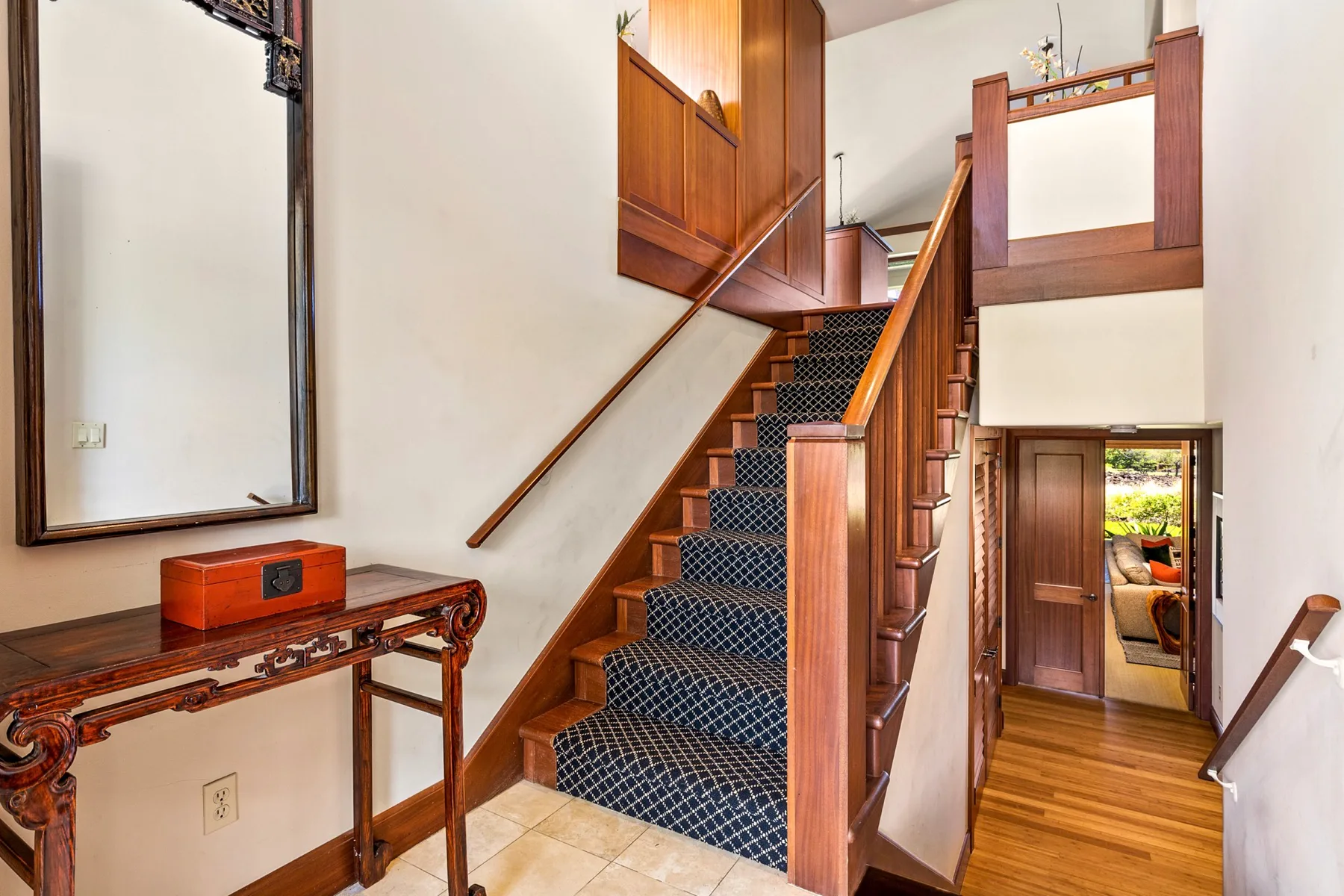 A wooden staircase with dark carpet rises beside a narrow entry hall.