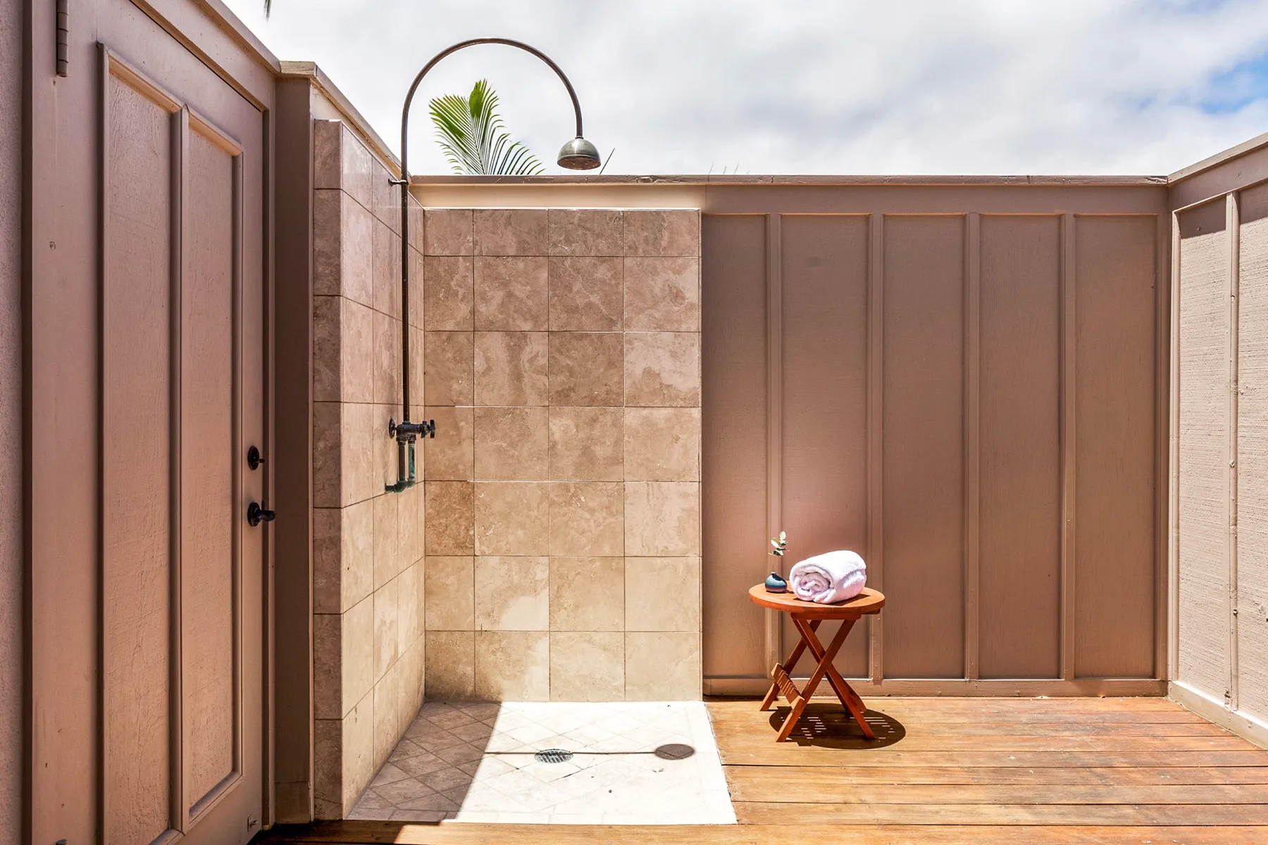 An outdoor shower area has tiled walls, a rainfall showerhead, and a small wooden table.