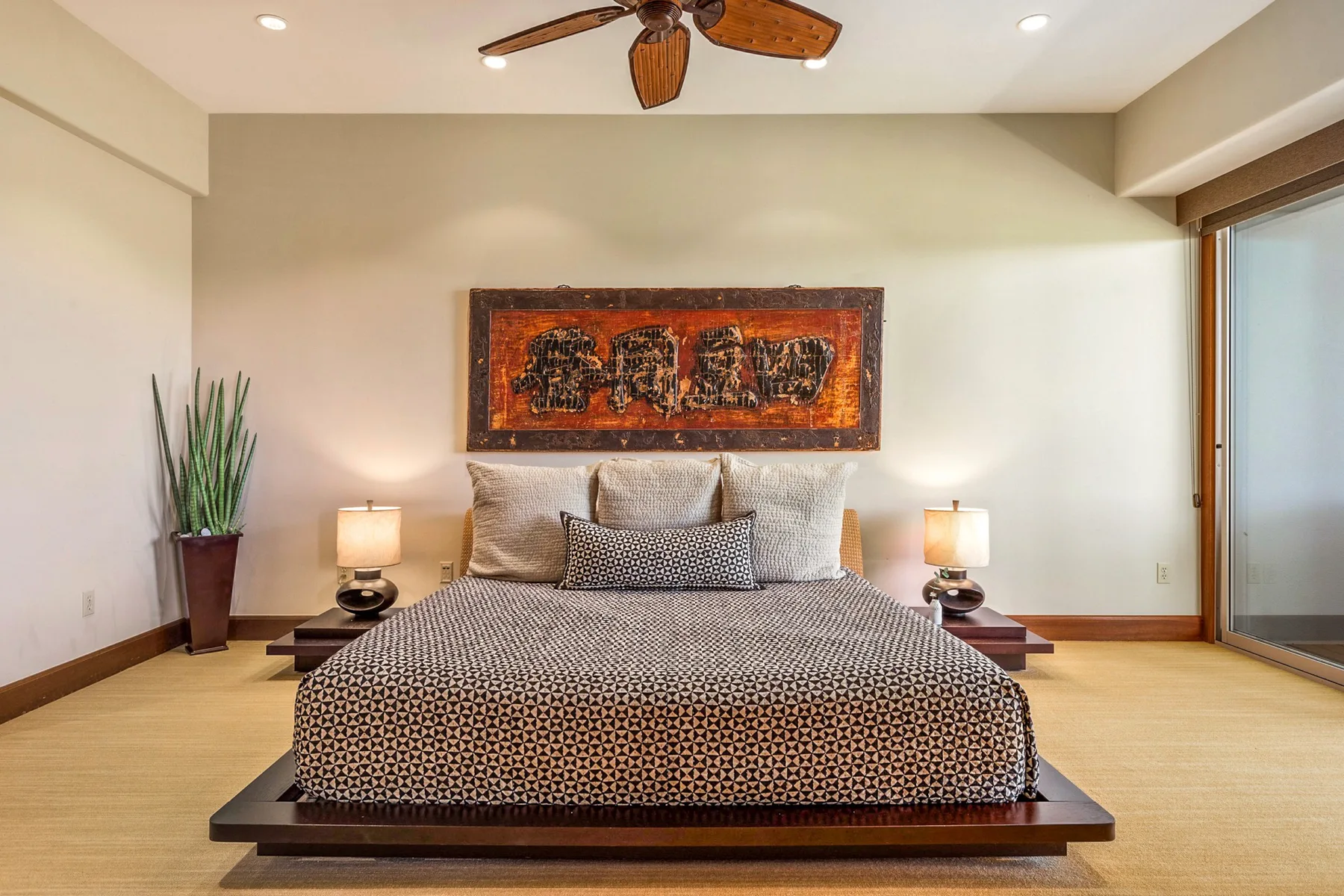 A bedroom with a large bed beneath framed artwork and a ceiling fan.