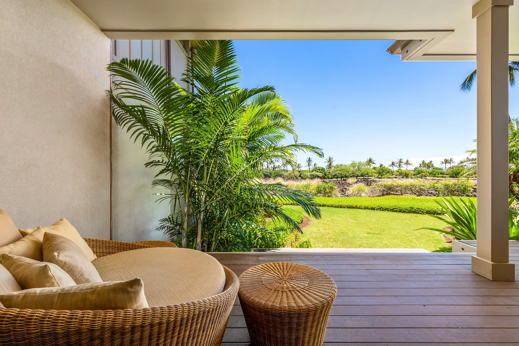 A covered patio with wicker seating overlooks a green lawn and palm trees.