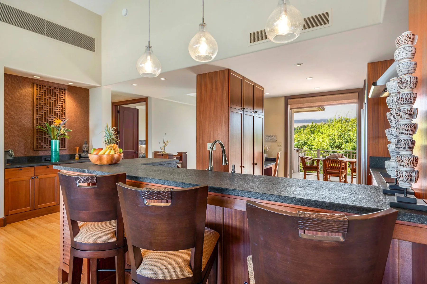 A modern kitchen with a wide counter, seating, and pendant lights.