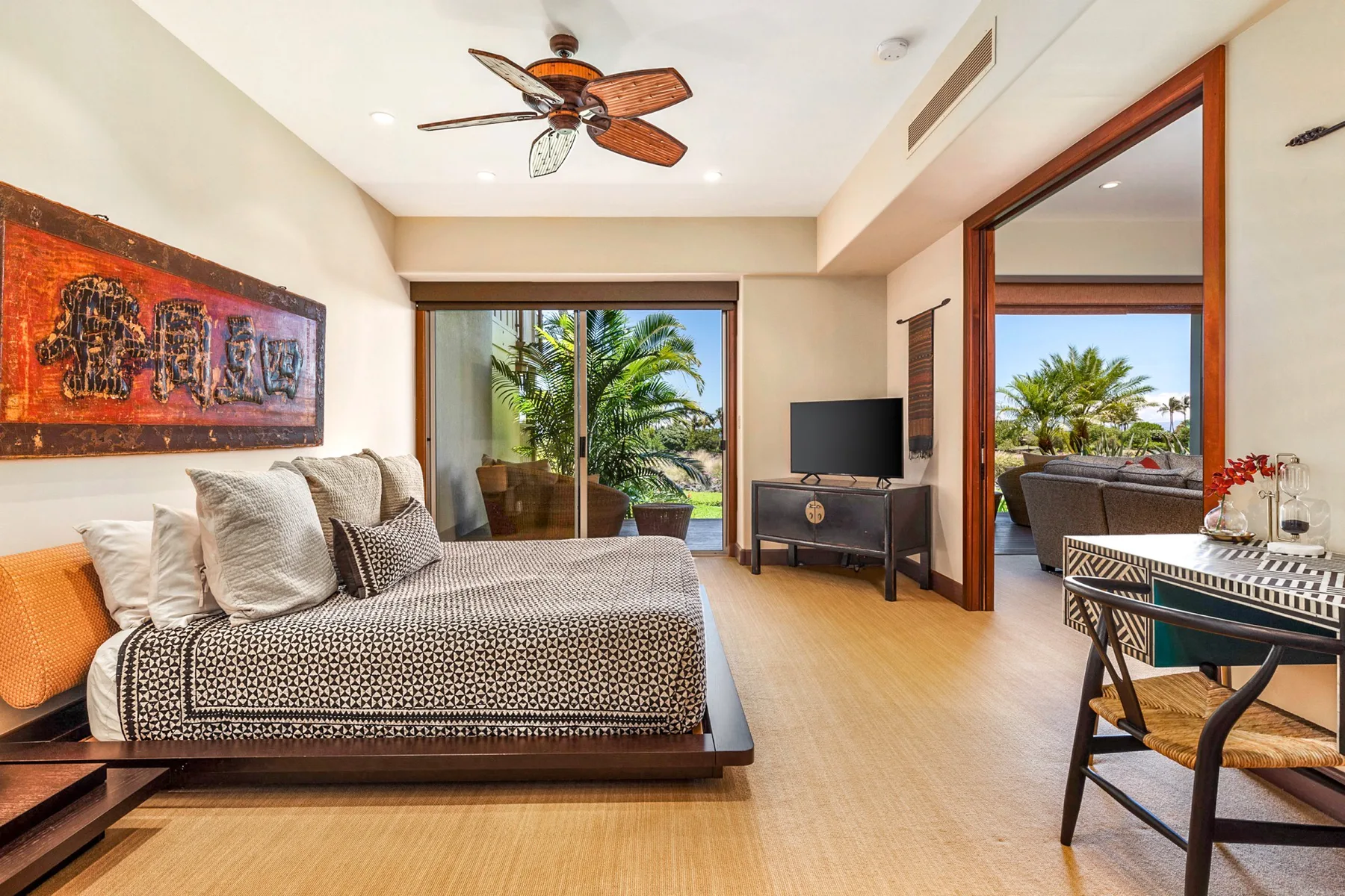 A bedroom with a bed beside wide glass doors overlooking palm trees.
