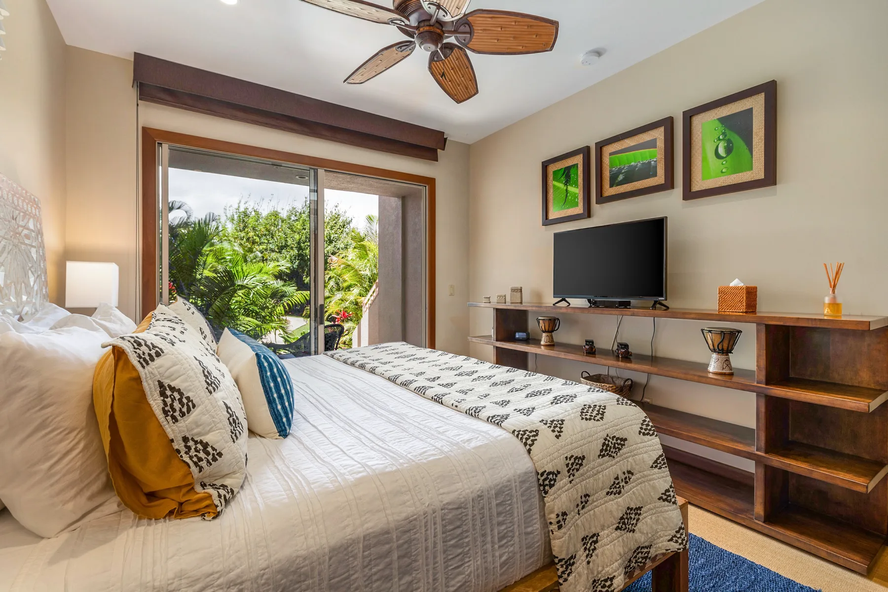 A bedroom with a bed facing a television and a large window overlooking greenery.