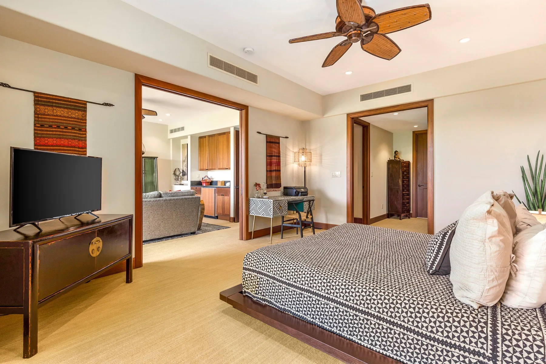 A bedroom with a patterned bed, television, and an open doorway to the adjoining living area.