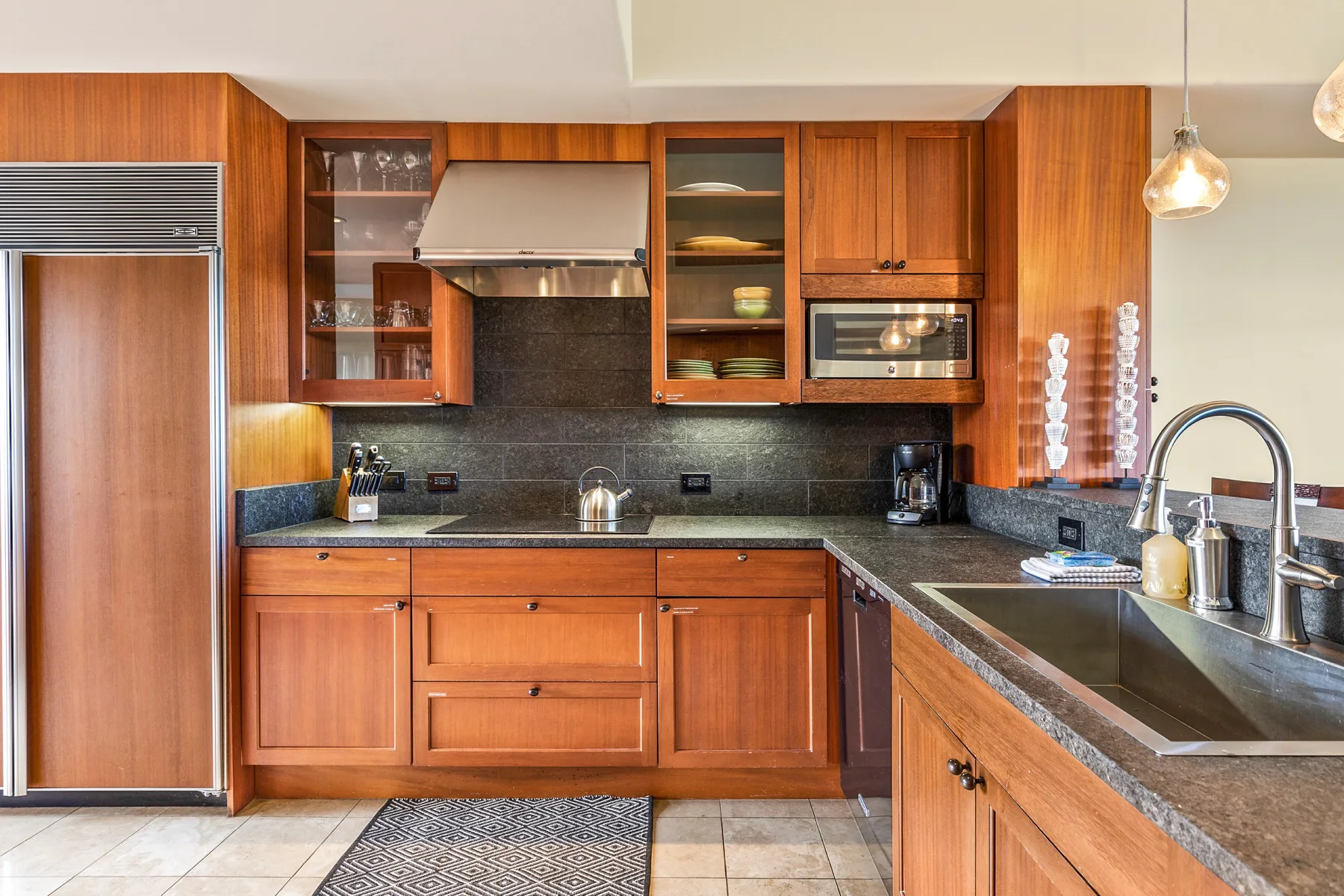 A kitchen with wooden cabinets, dark countertops, and a stainless steel refrigerator.