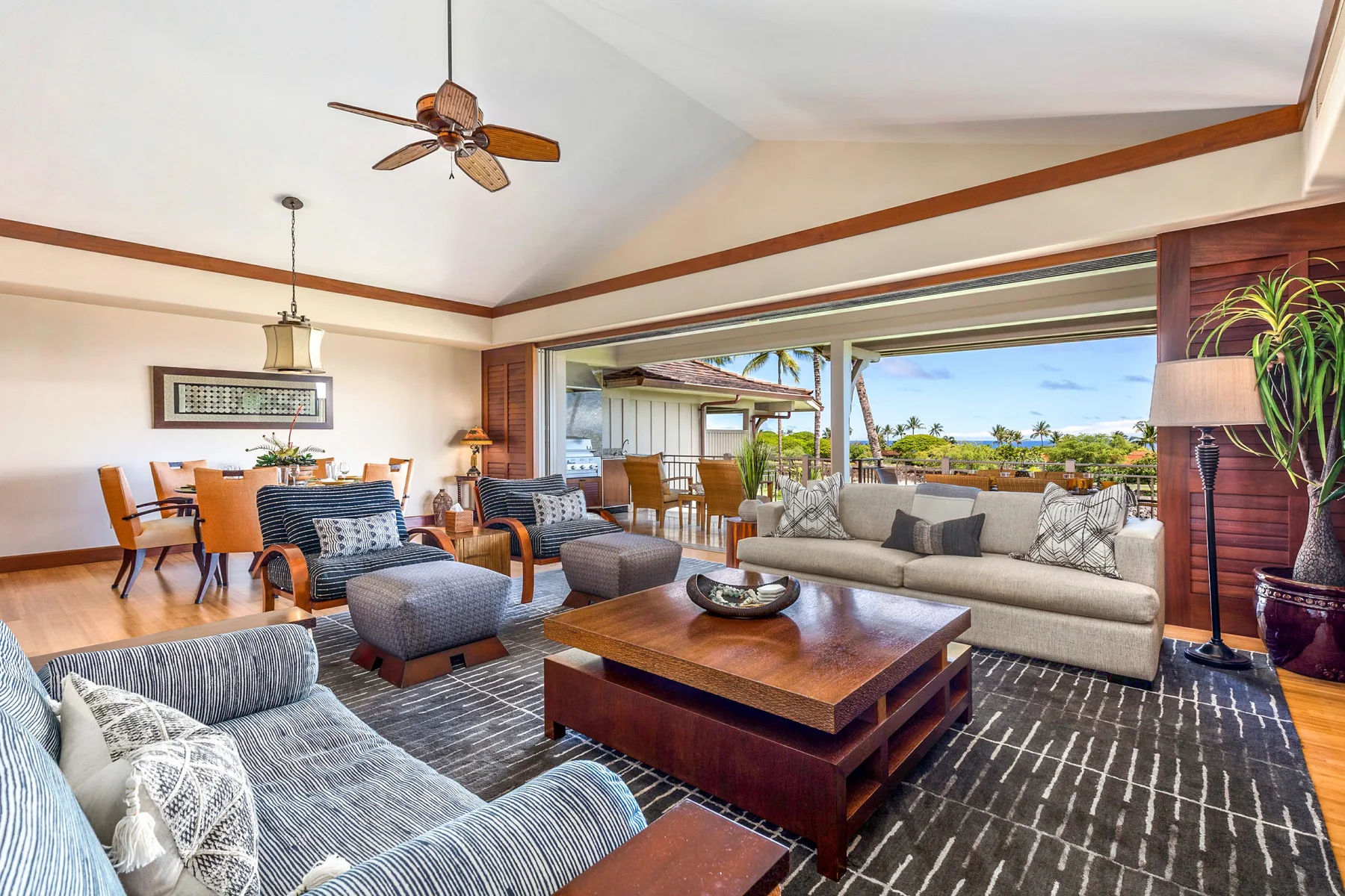 A living room with seating around a wooden coffee table and a view through open doors.