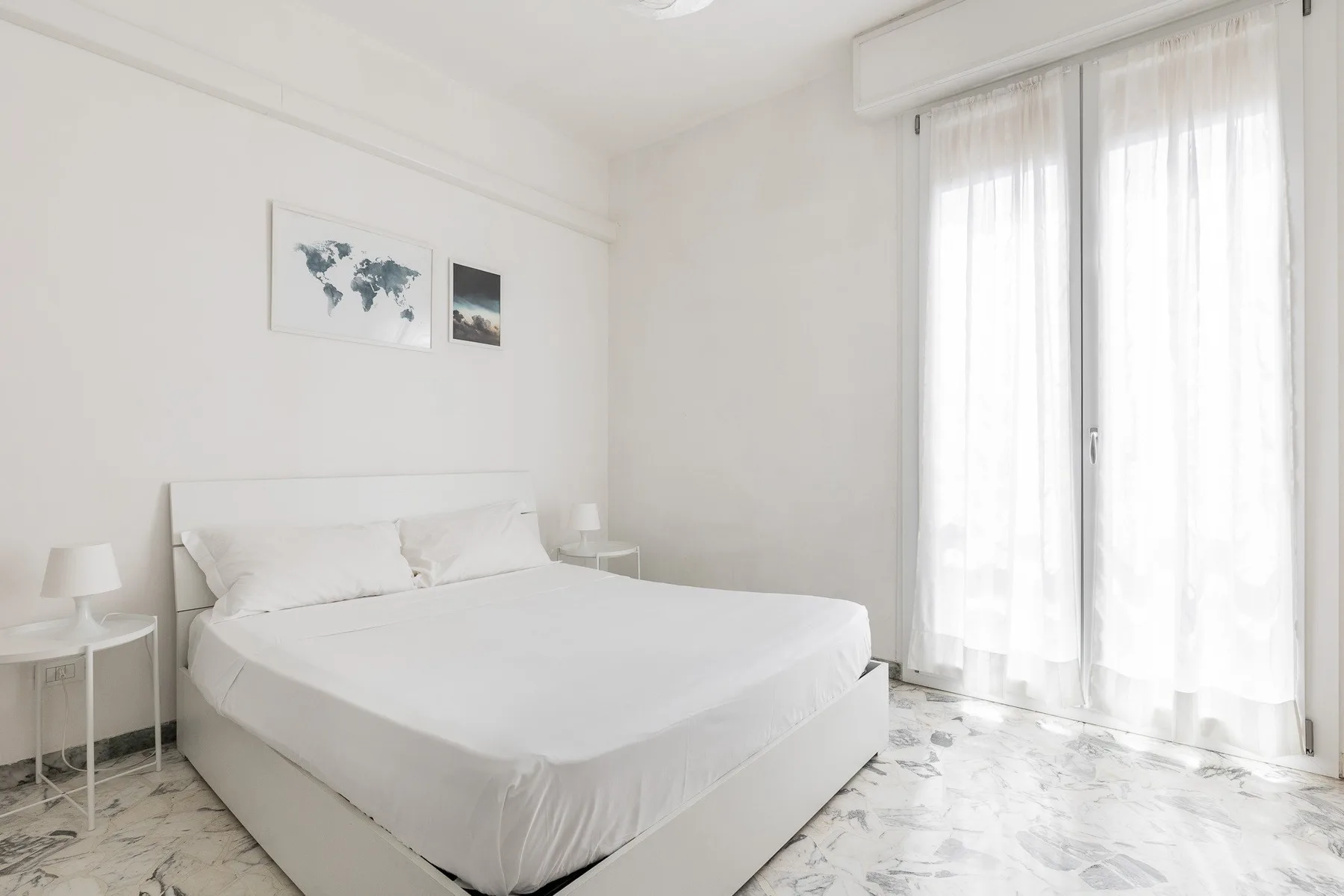 A bright bedroom with a neatly made bed and sheer curtains.