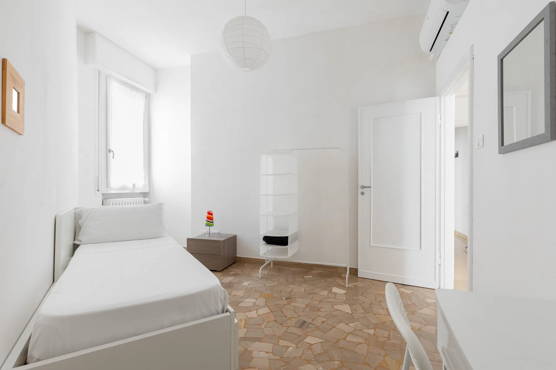 Un dormitorio blanco y luminoso con una cama, una ventana y suelo de baldosas.