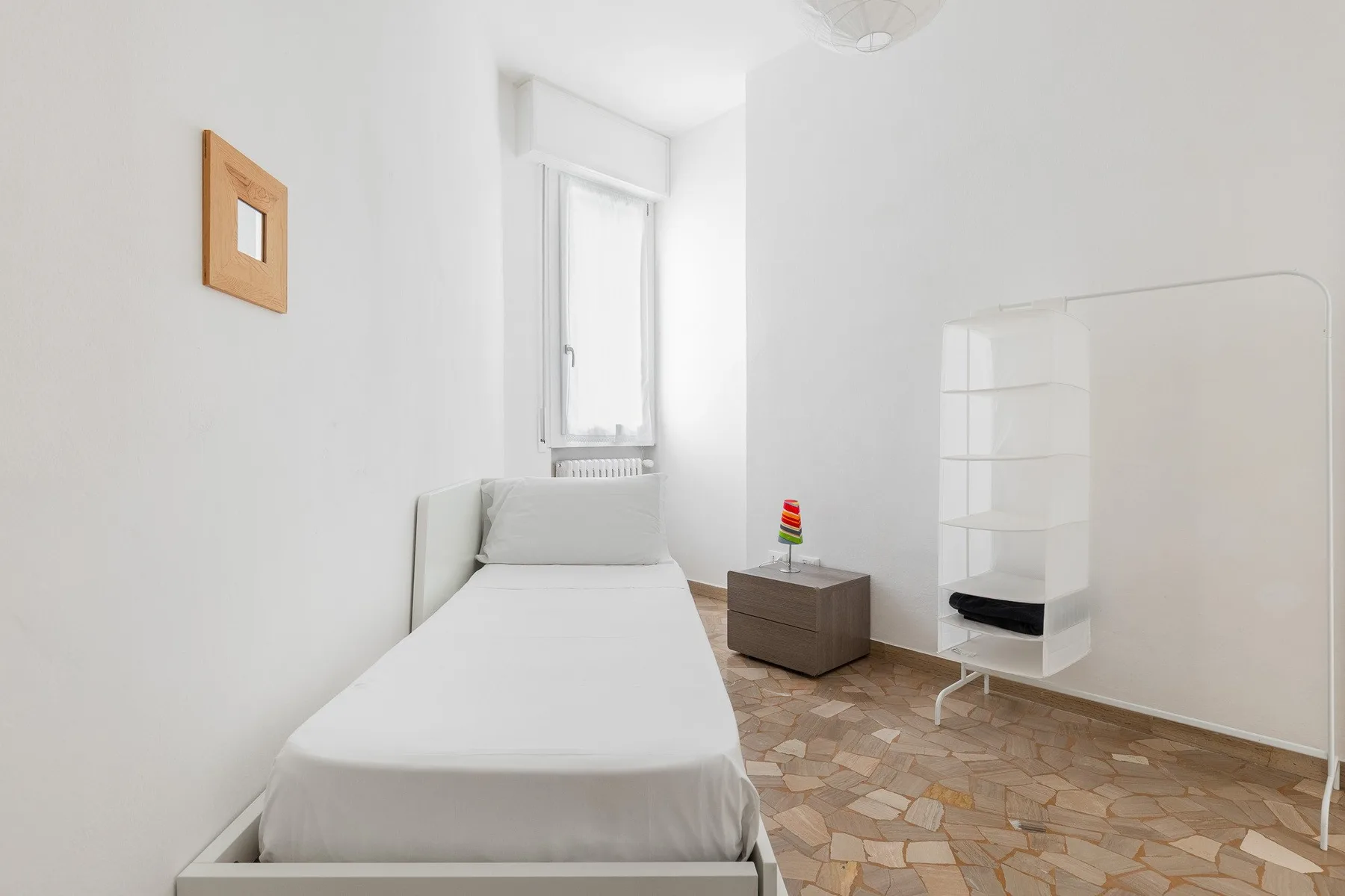 A bright bedroom with a single bed and a white shelving unit.