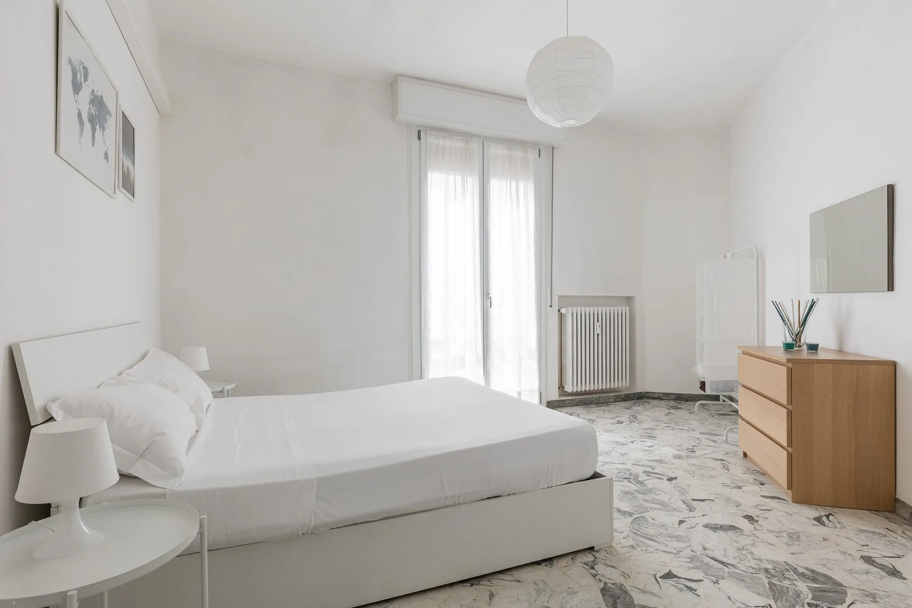 A bright bedroom with a bed, sheer curtains, and a wooden dresser.