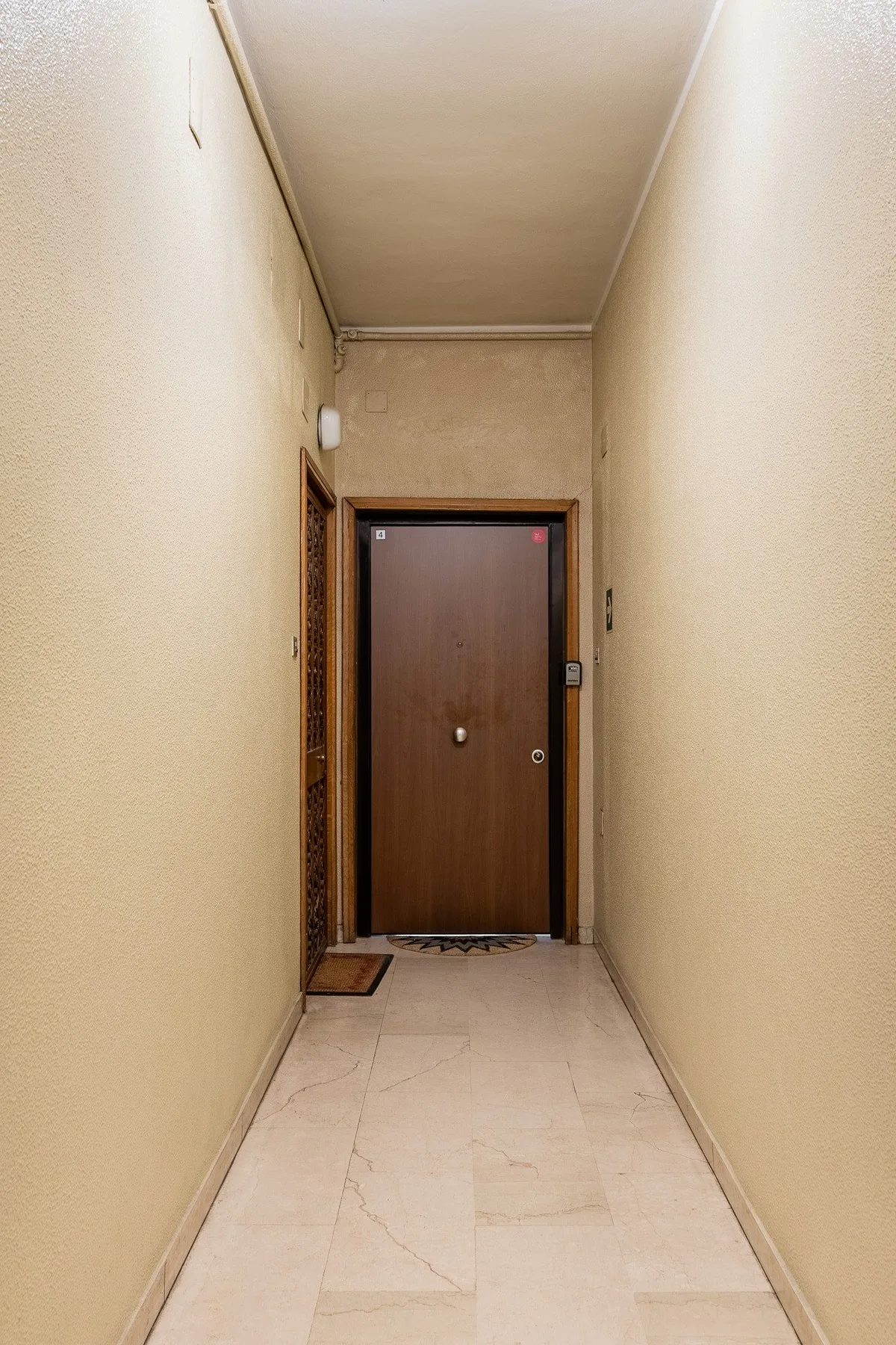 Un pasillo interior estrecho conduce a una puerta marrón cerrada.