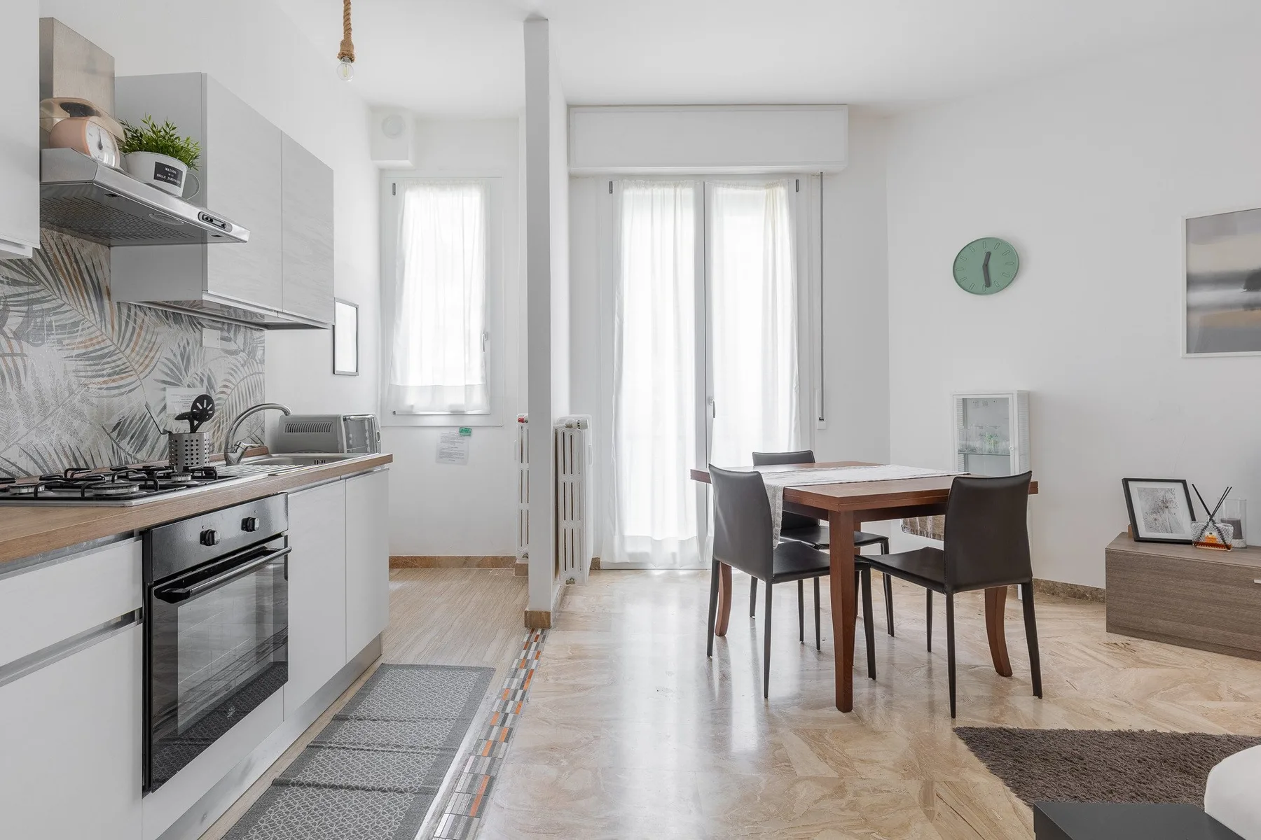 A bright open-plan kitchen and dining area with a table beside tall windows.