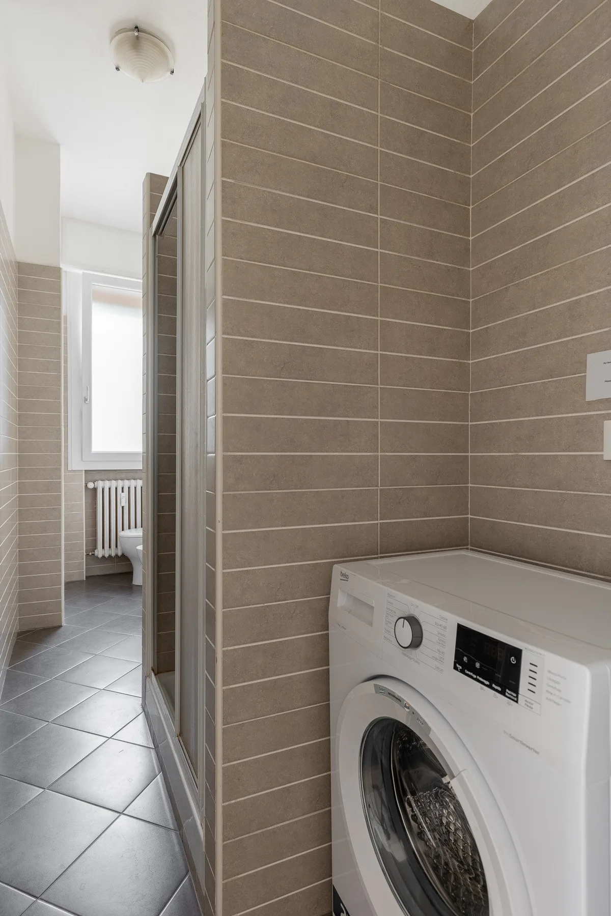 Una zona de baño con azulejos, una lavadora y una ducha.