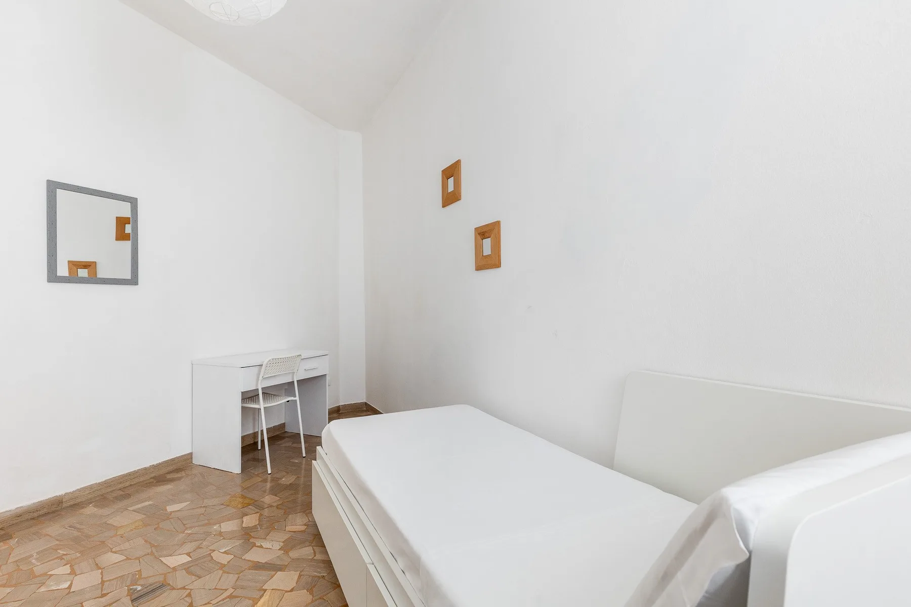Un dormitorio luminoso con una cama y un pequeño escritorio junto a la pared.