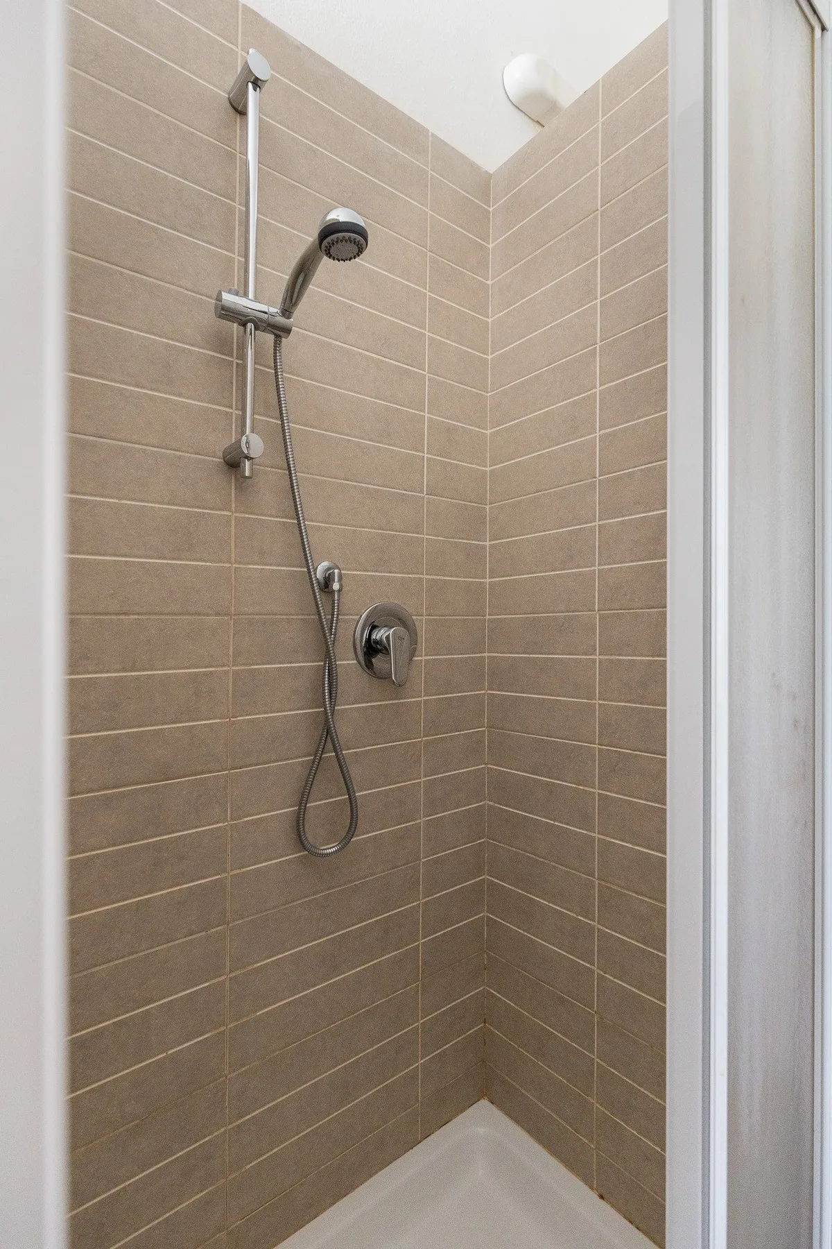 Una ducha con azulejos, cabezal de mano y controles montados en la pared.