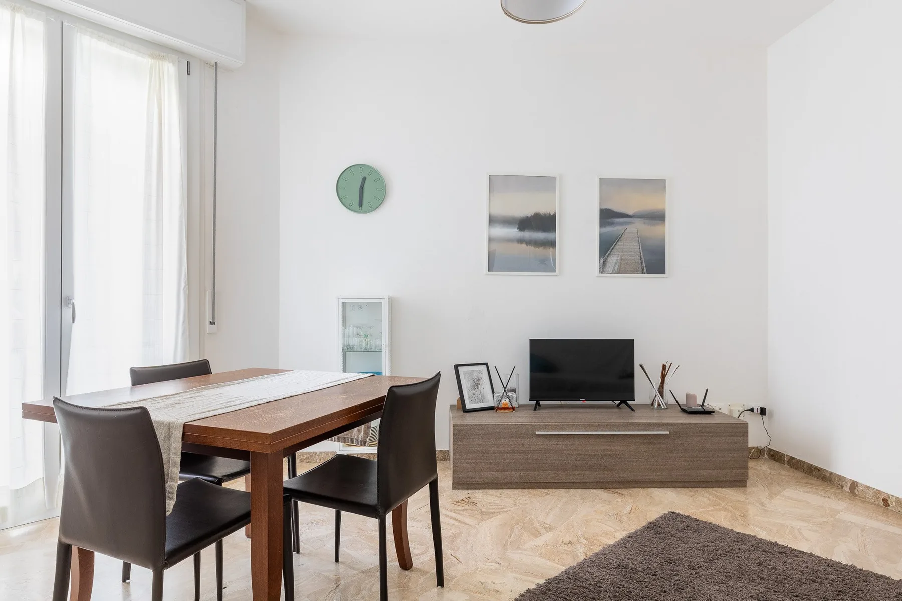 A bright dining and living area with a wooden table and television.