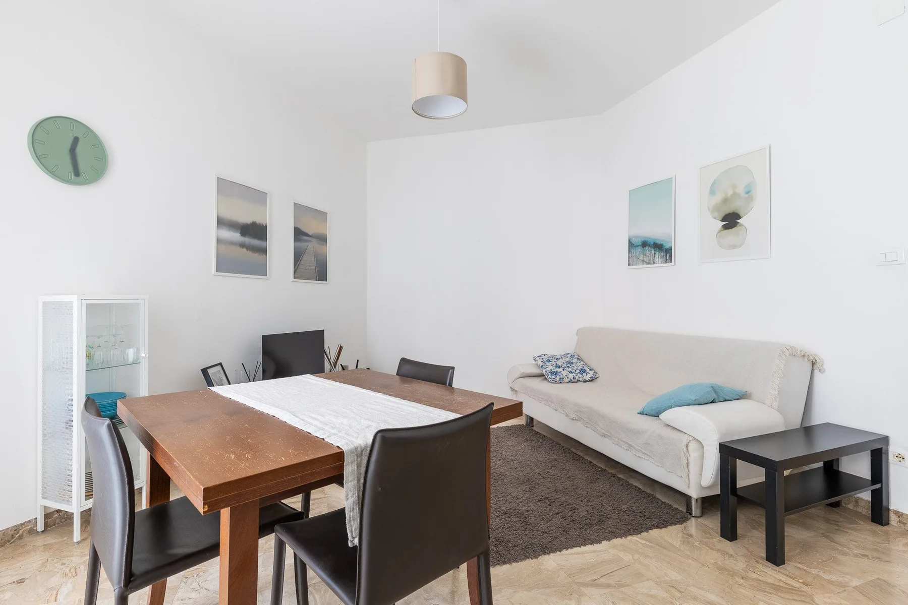 A bright living and dining area with a wooden table and pale sofa.