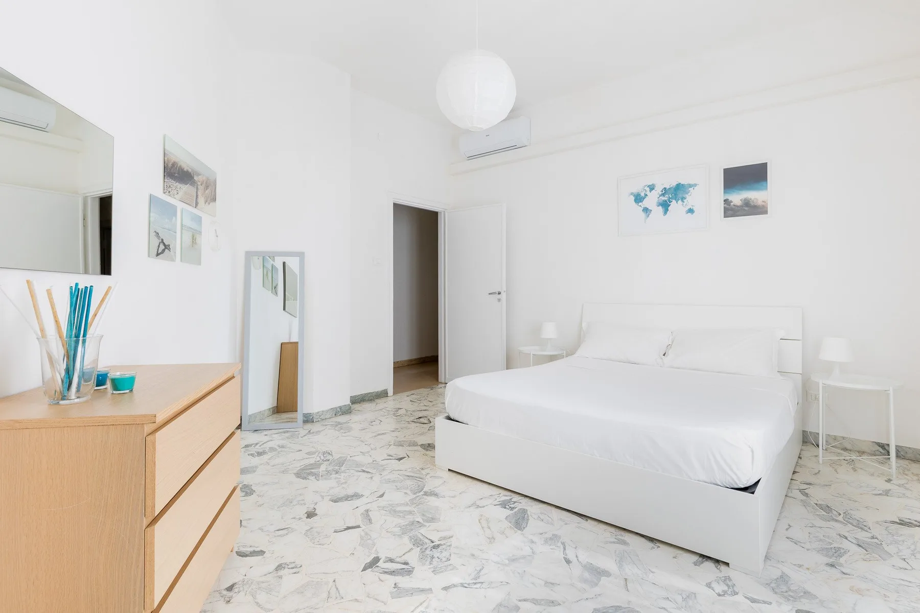 Un dormitorio luminoso con una cama blanca, mesillas y cuadros en la pared.