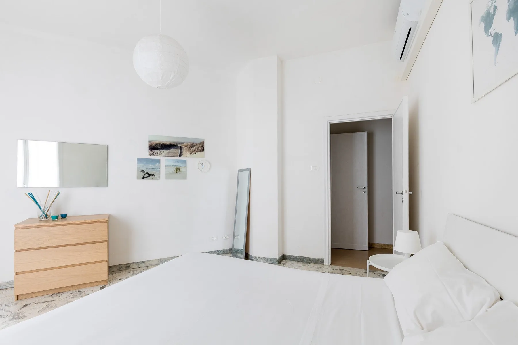 Un dormitorio luminoso con una cama, una cómoda y una puerta abierta.