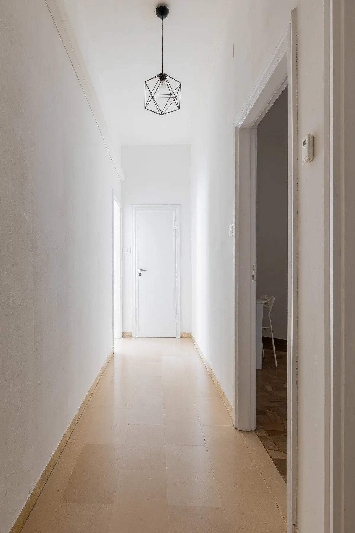 Un pasillo luminoso con una lámpara geométrica y una puerta cerrada al fondo.