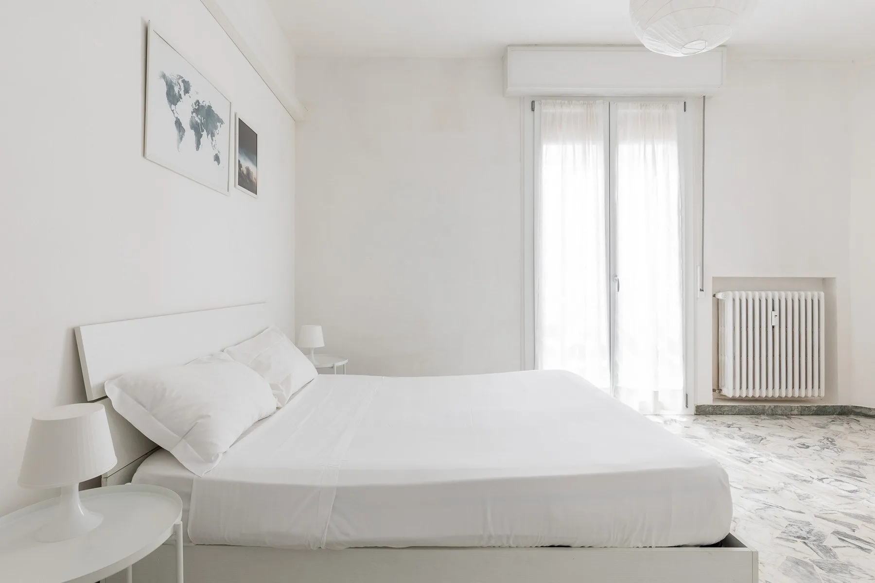 Un dormitorio luminoso con una cama blanca y cortinas translúcidas en la ventana.