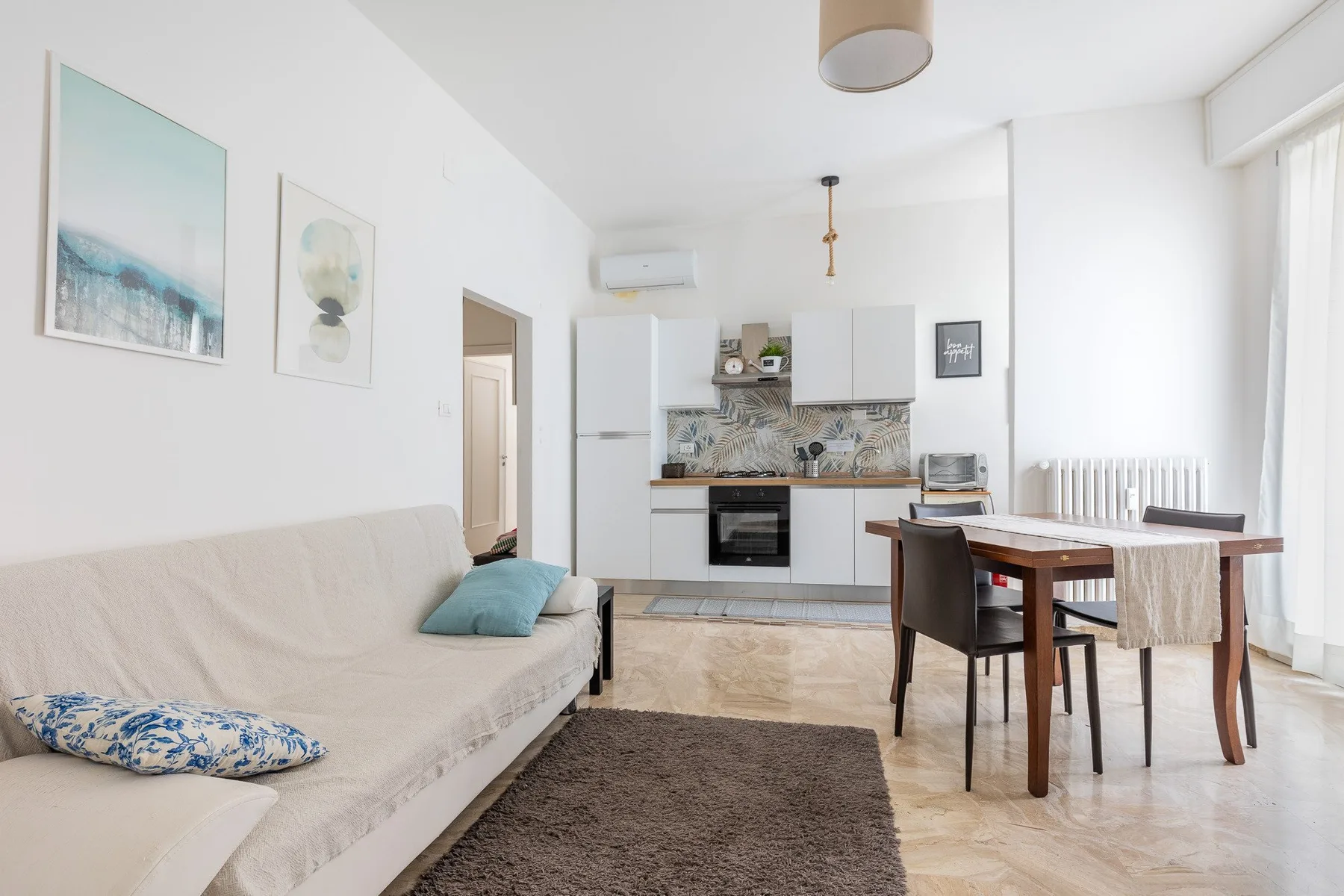 Una luminosa sala de estar y comedor con una cocina compacta y asientos claros.