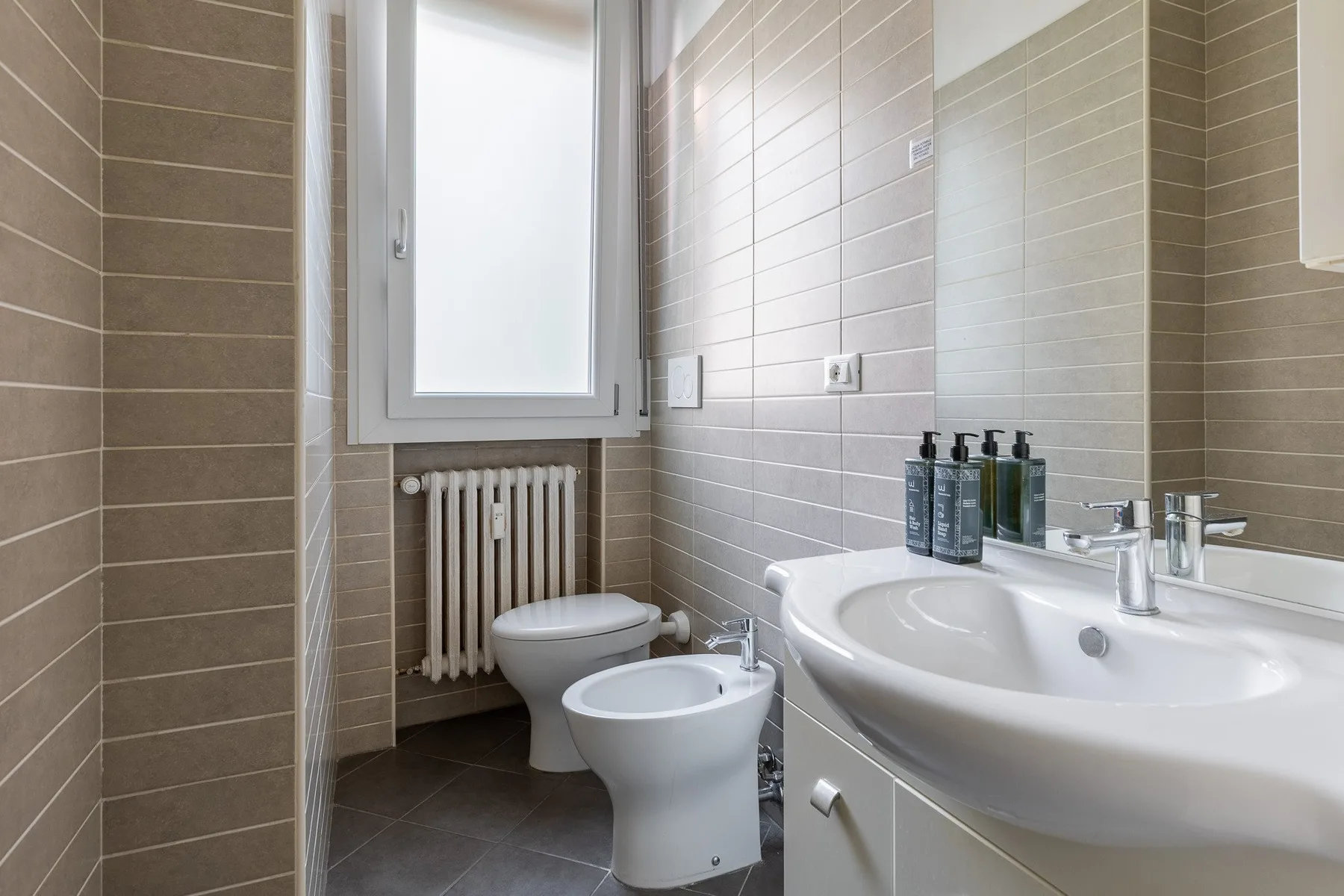 Un baño alicatado con lavabo, inodoro y bidé bajo una ventana translúcida.