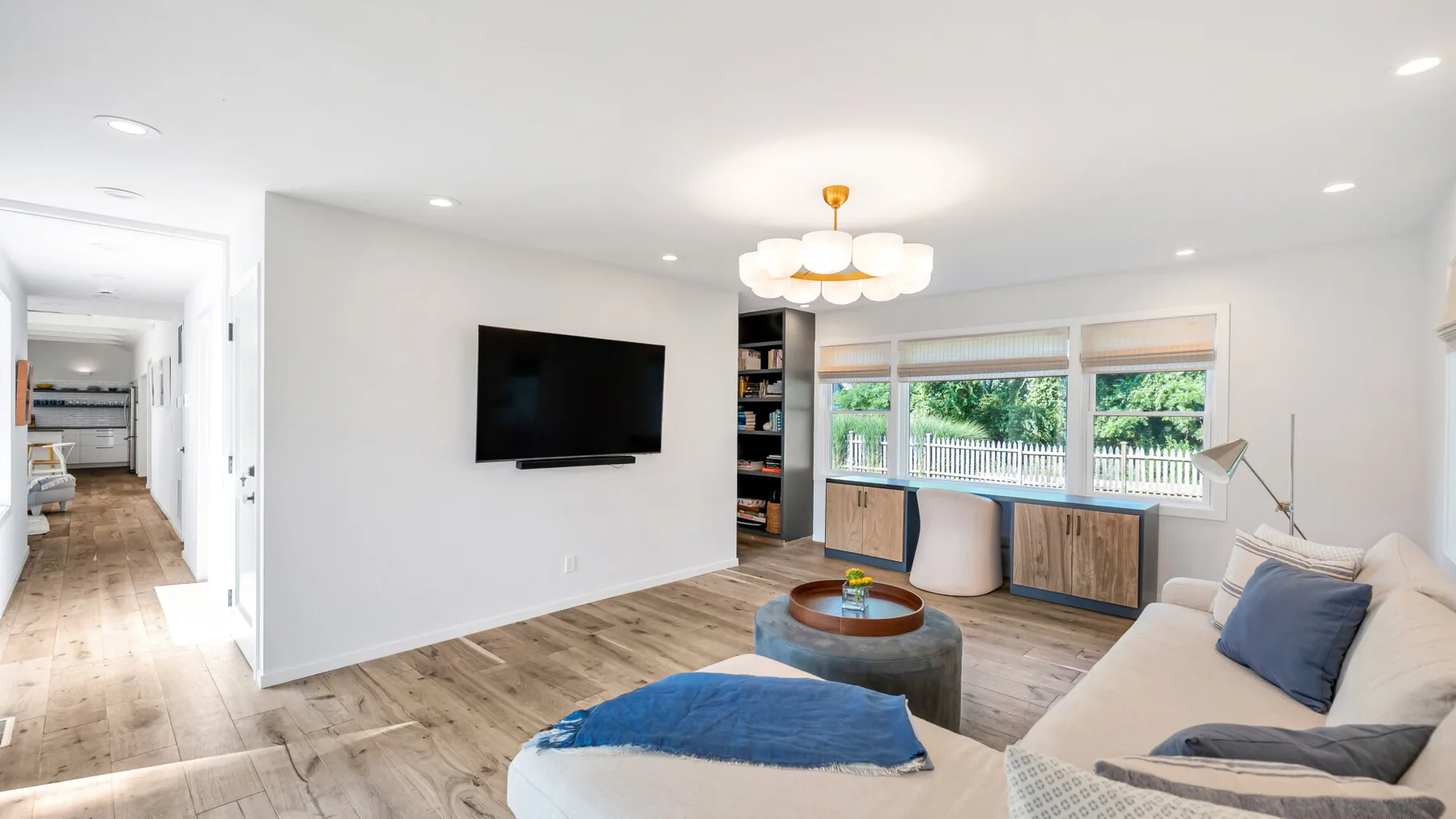 Una sala luminosa con televisor, ventanas grandes y asientos.