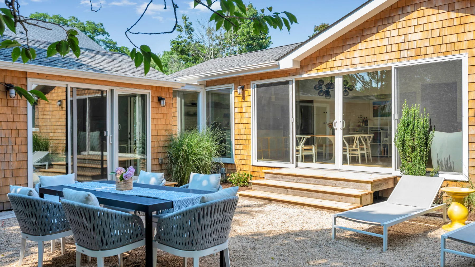 An outdoor patio with a dining table, seating, and a lounge chair beside the house.
