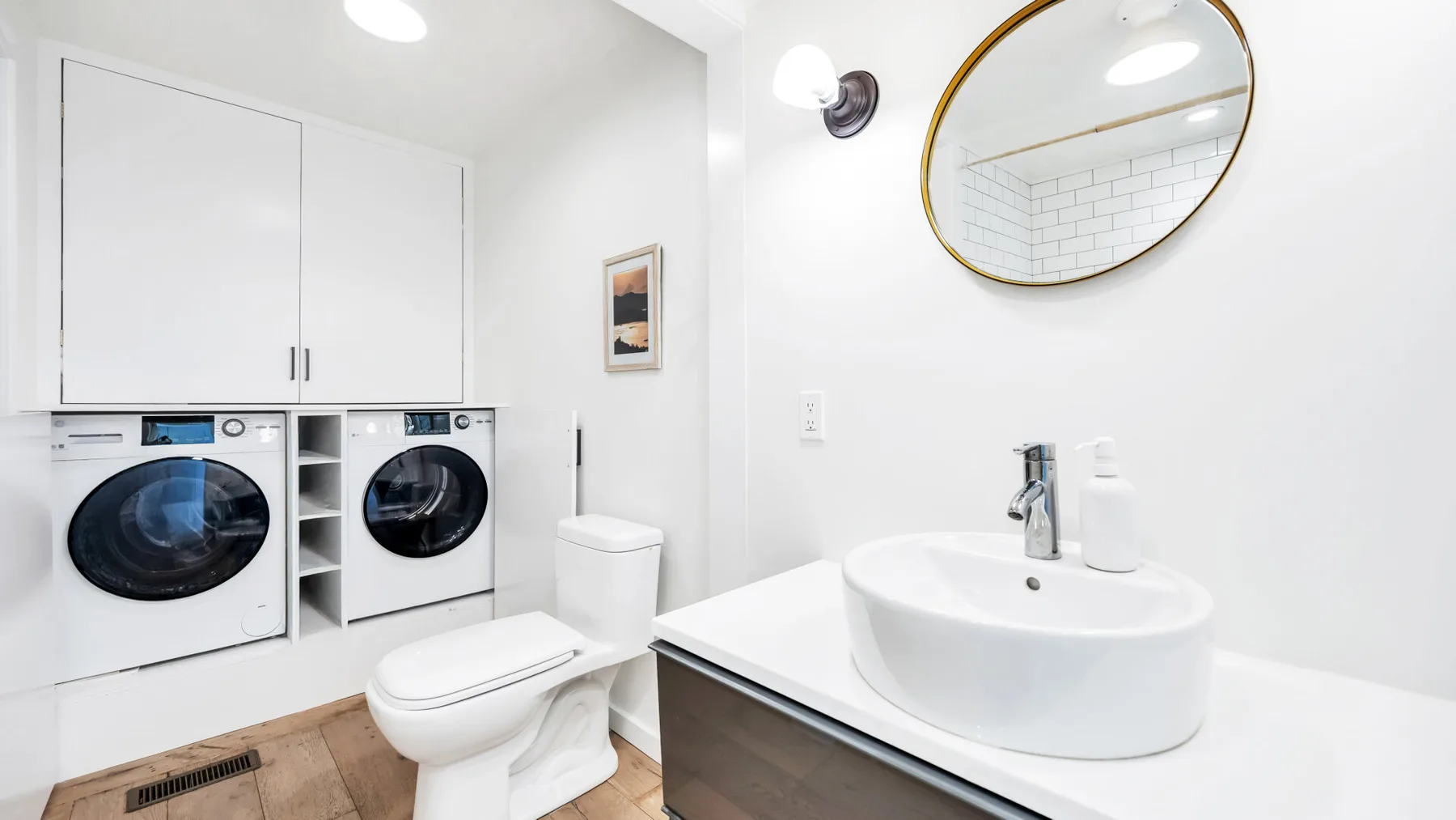 Un baño luminoso con lavabo, inodoro y electrodomésticos de lavandería bajo armarios blancos.