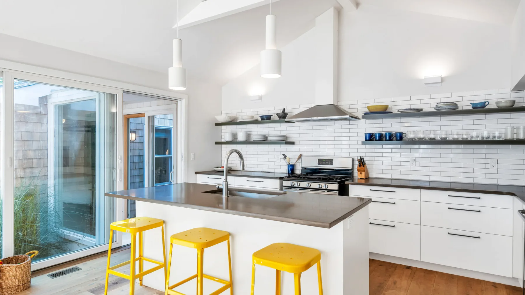 Una cocina luminosa con isla central, taburetes amarillos y puertas corredizas de vidrio.