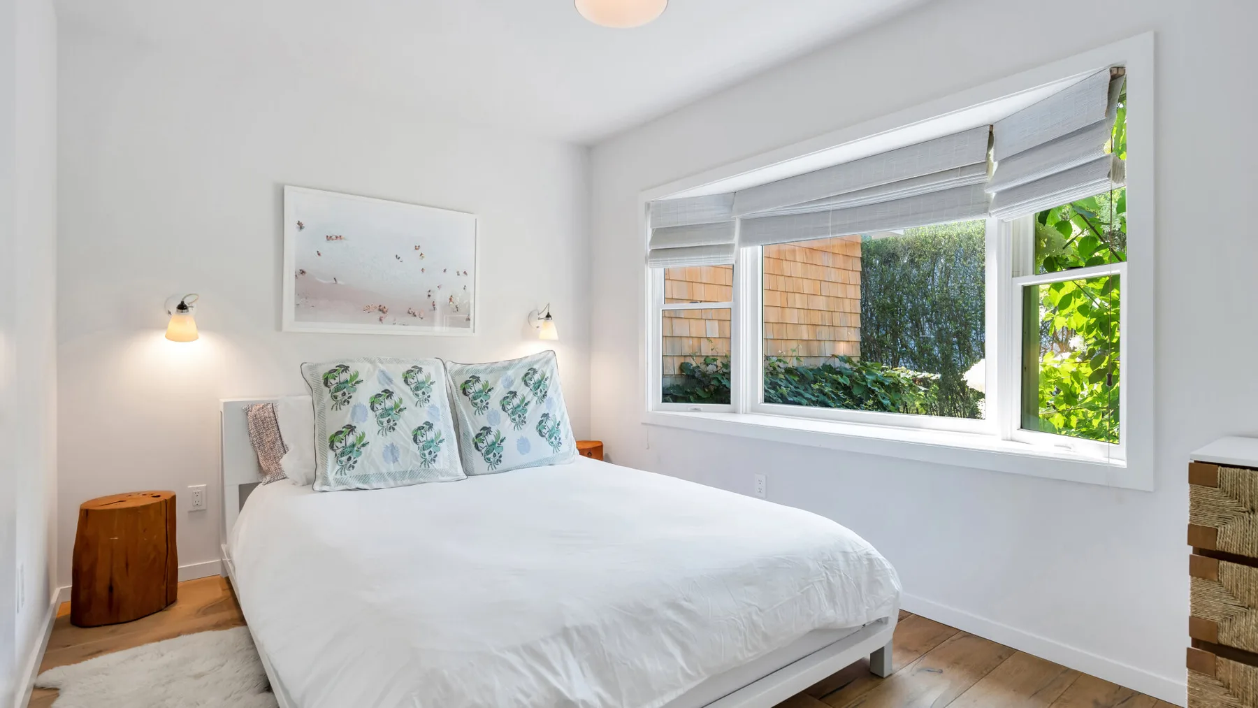 Un dormitorio luminoso con una cama tendida bajo una ventana amplia.