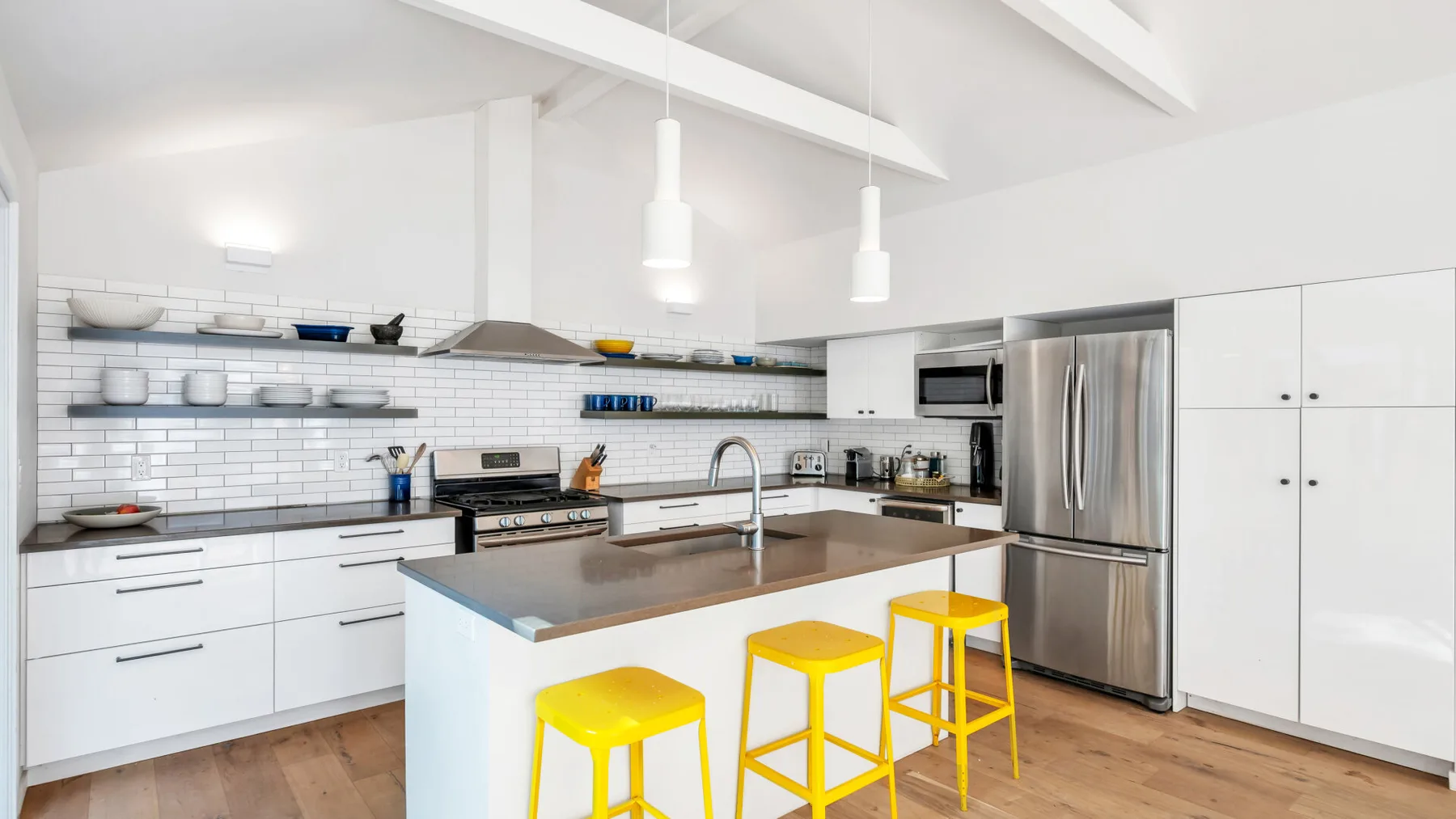 Una cocina luminosa con gabinetes blancos, una isla central y taburetes amarillos.