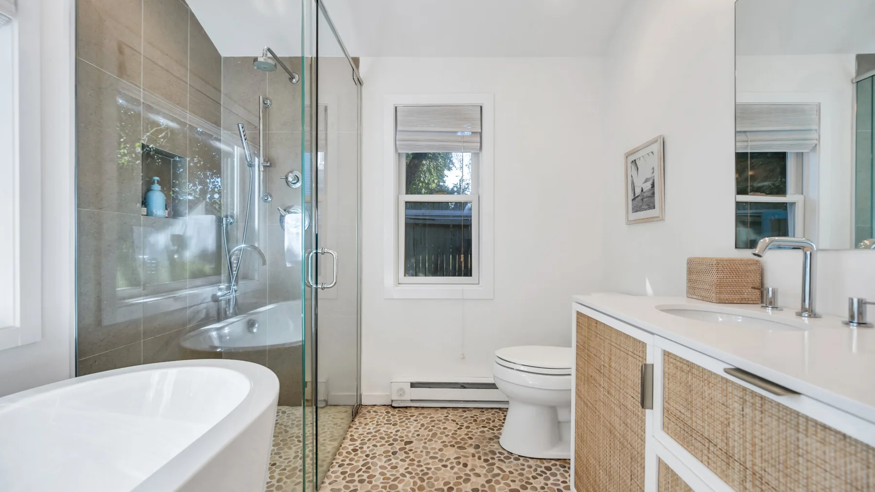 Un baño luminoso con ducha de vidrio, bañera y tocador.