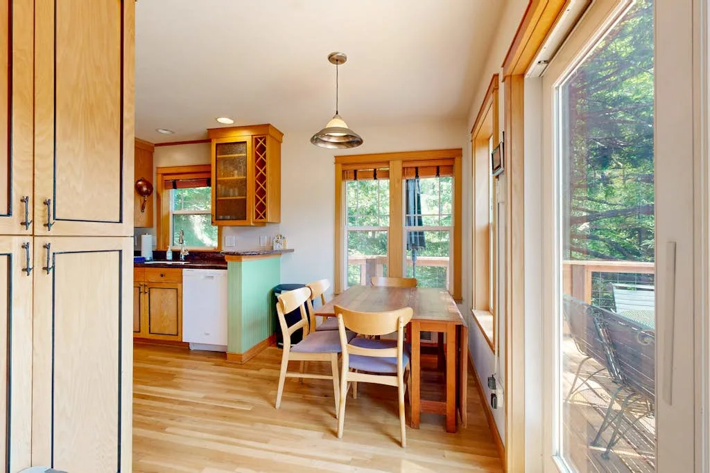 Una cocina luminosa con comedor y una mesa de madera junto a grandes ventanas.