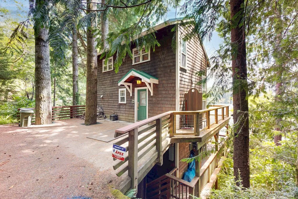A raised wooden cabin among trees, with a long deck and green entrance door.