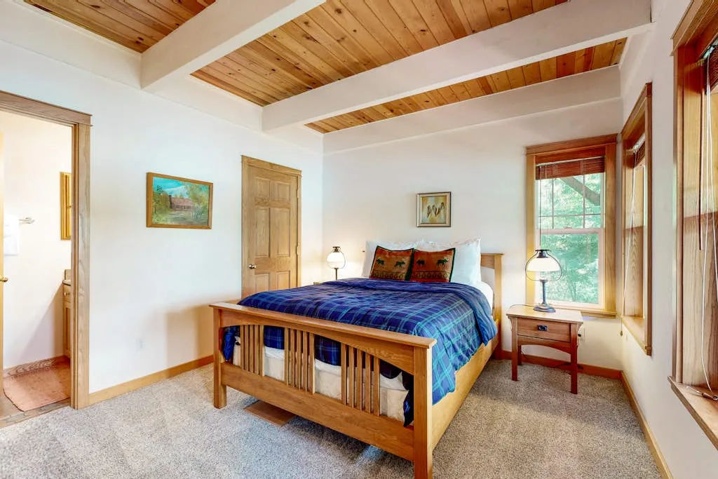 Un dormitorio con una cama de madera, ropa de cama azul y ventanas.