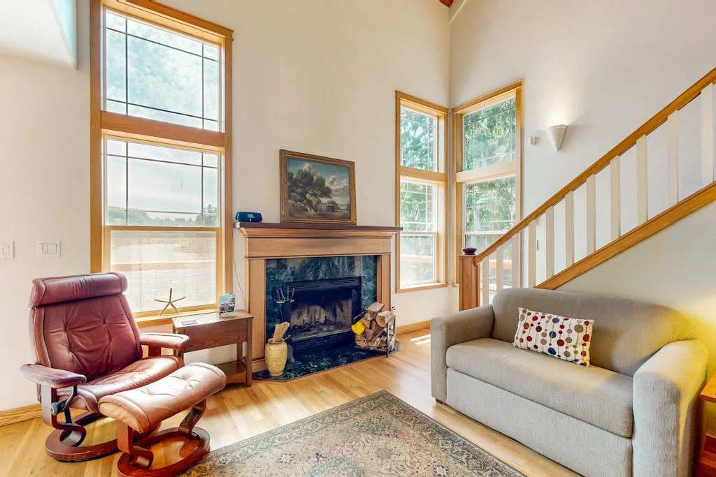 Una sala luminosa con chimenea, ventanas altas y asientos cómodos.