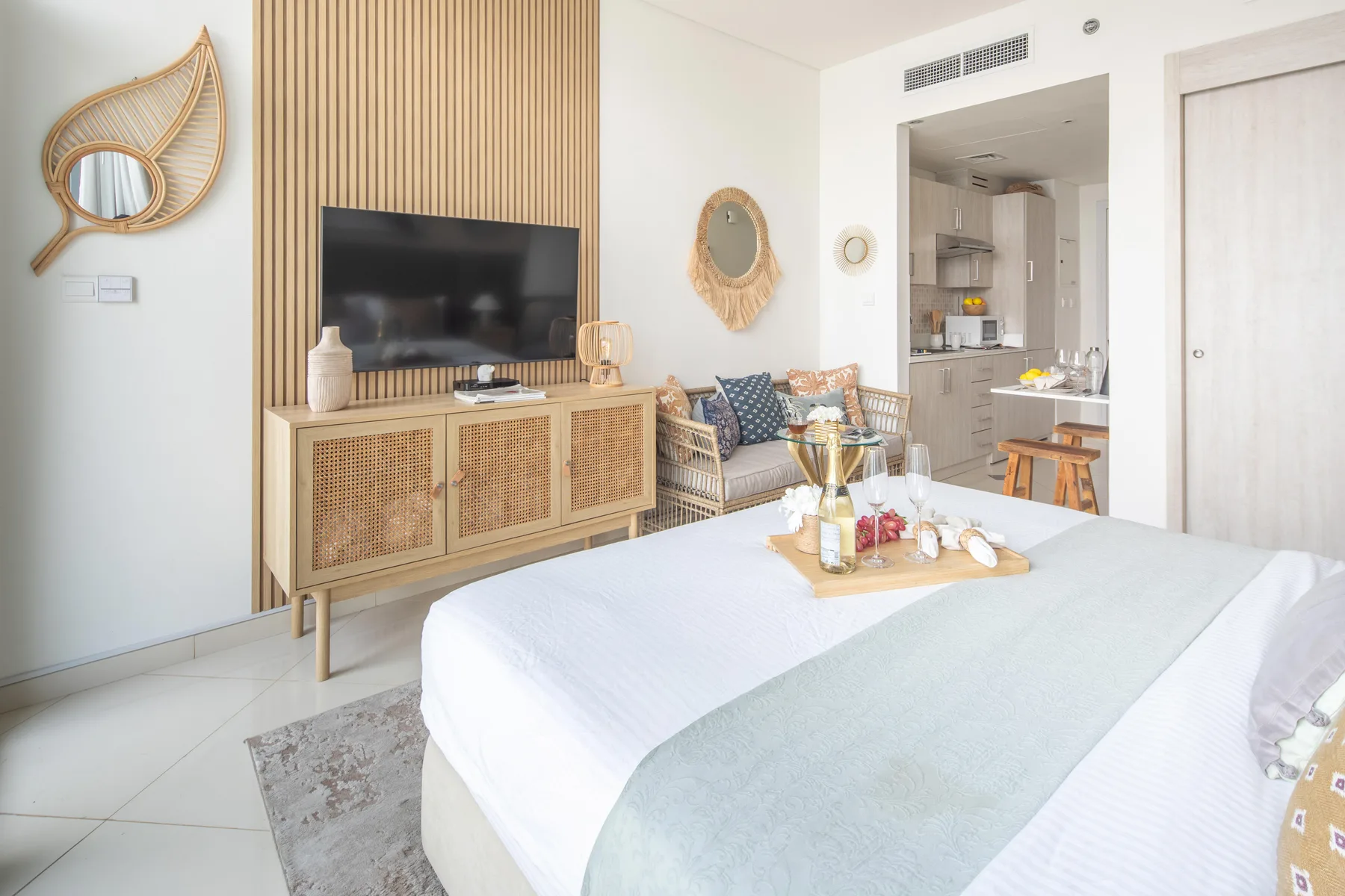 Un dormitorio luminoso con una cama grande, un mueble tejido y un televisor.