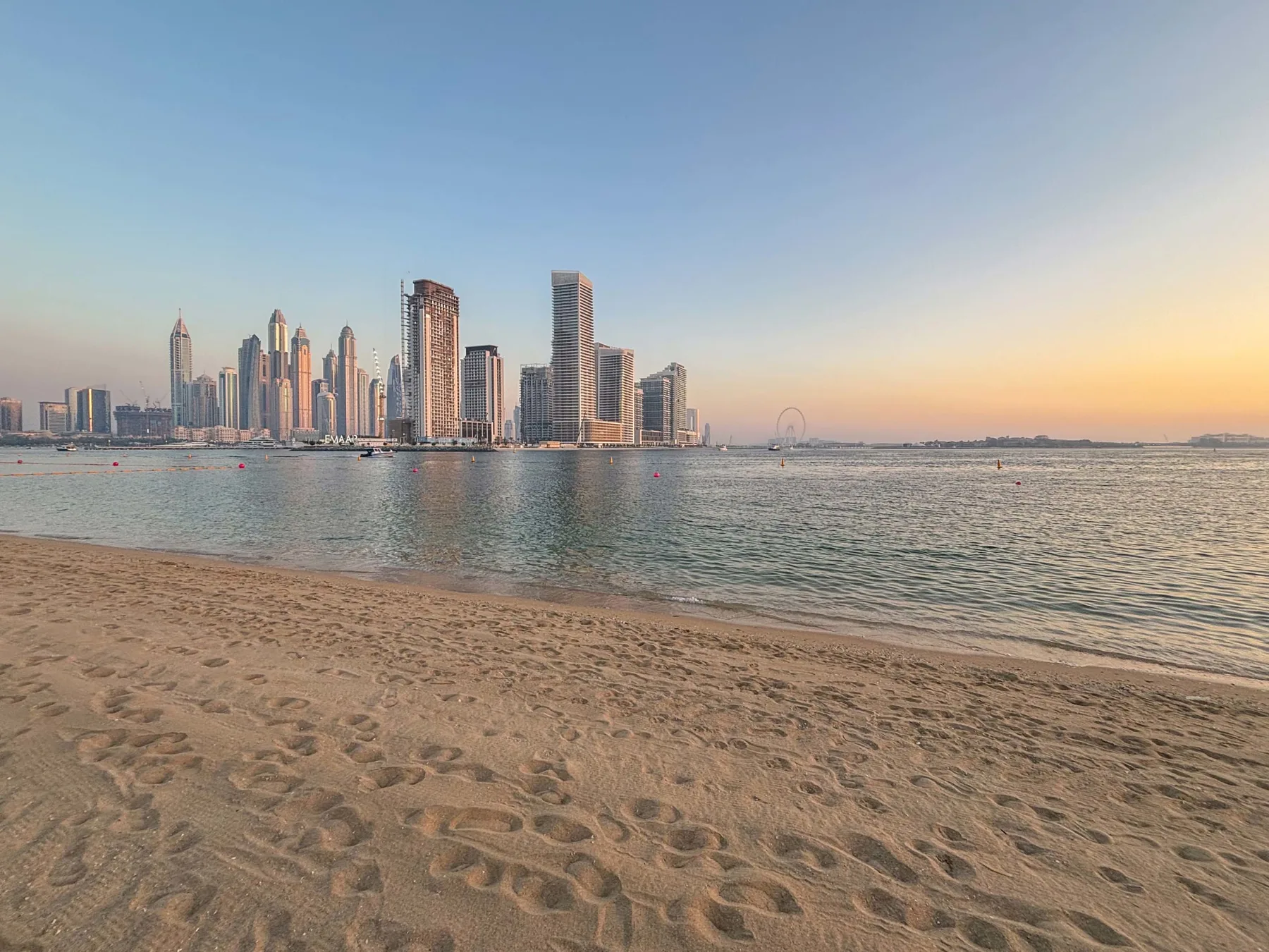 Una playa de arena da a aguas tranquilas y un horizonte urbano lejano.
