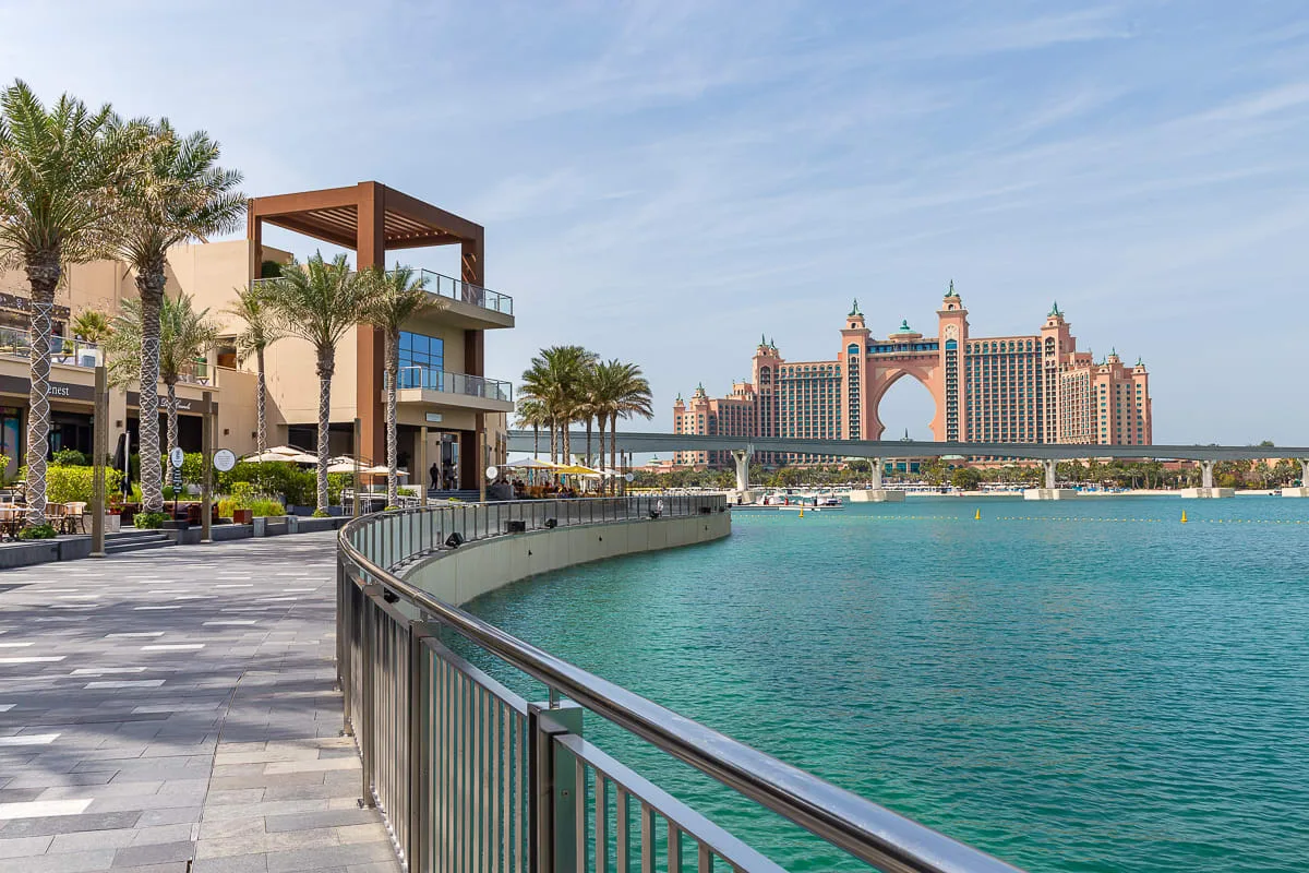 Un paseo junto al agua bordea la bahía turquesa, con un gran hotel al otro lado.
