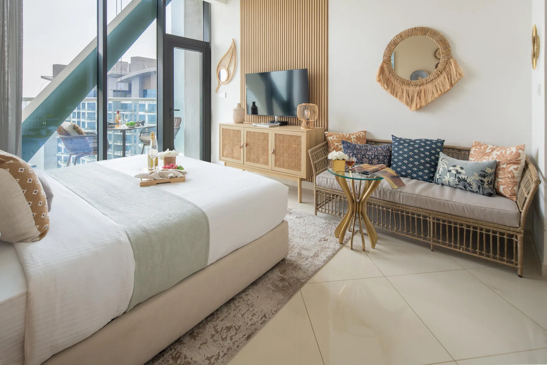 Un dormitorio luminoso con una cama grande, asientos estampados y un televisor.