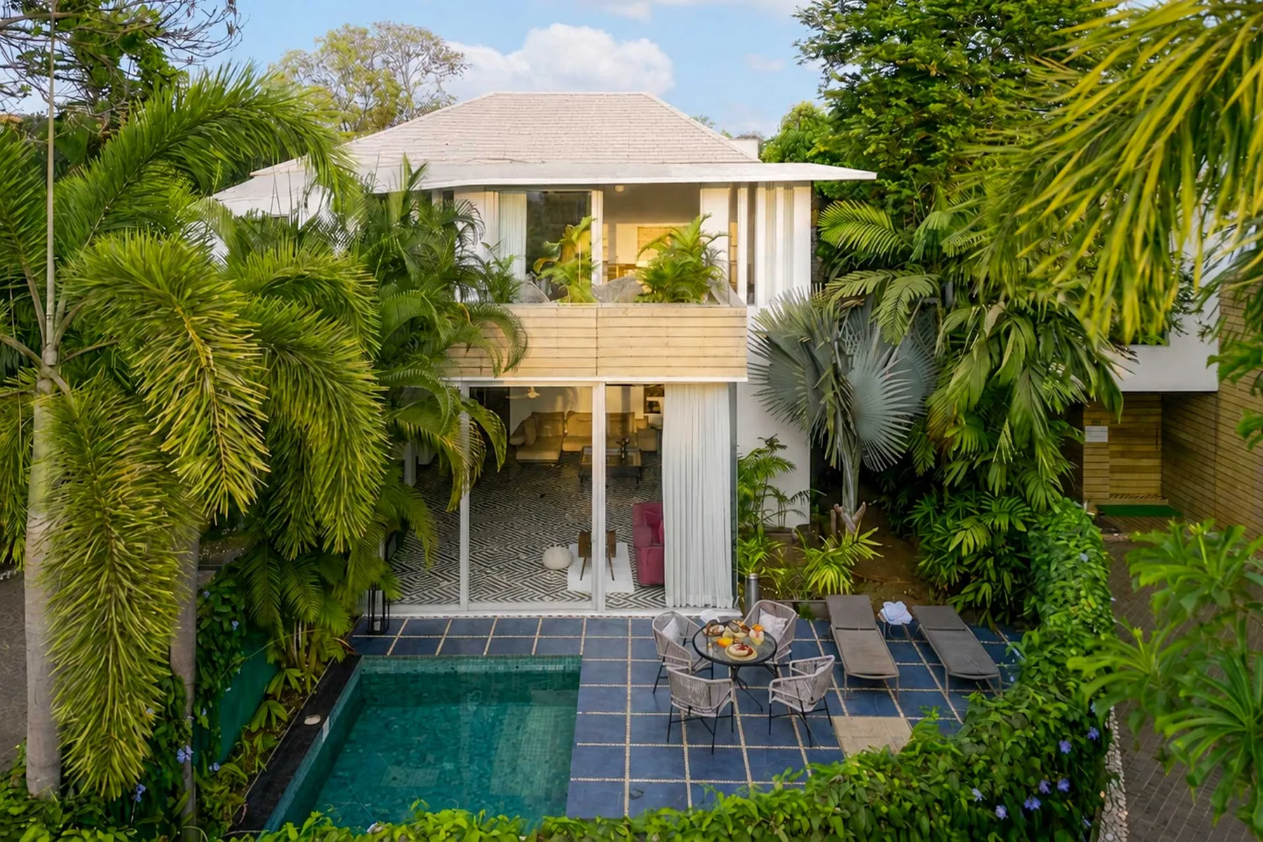 Una casa tropical da a un patio embaldosado con una pequeña piscina y asientos al aire libre.